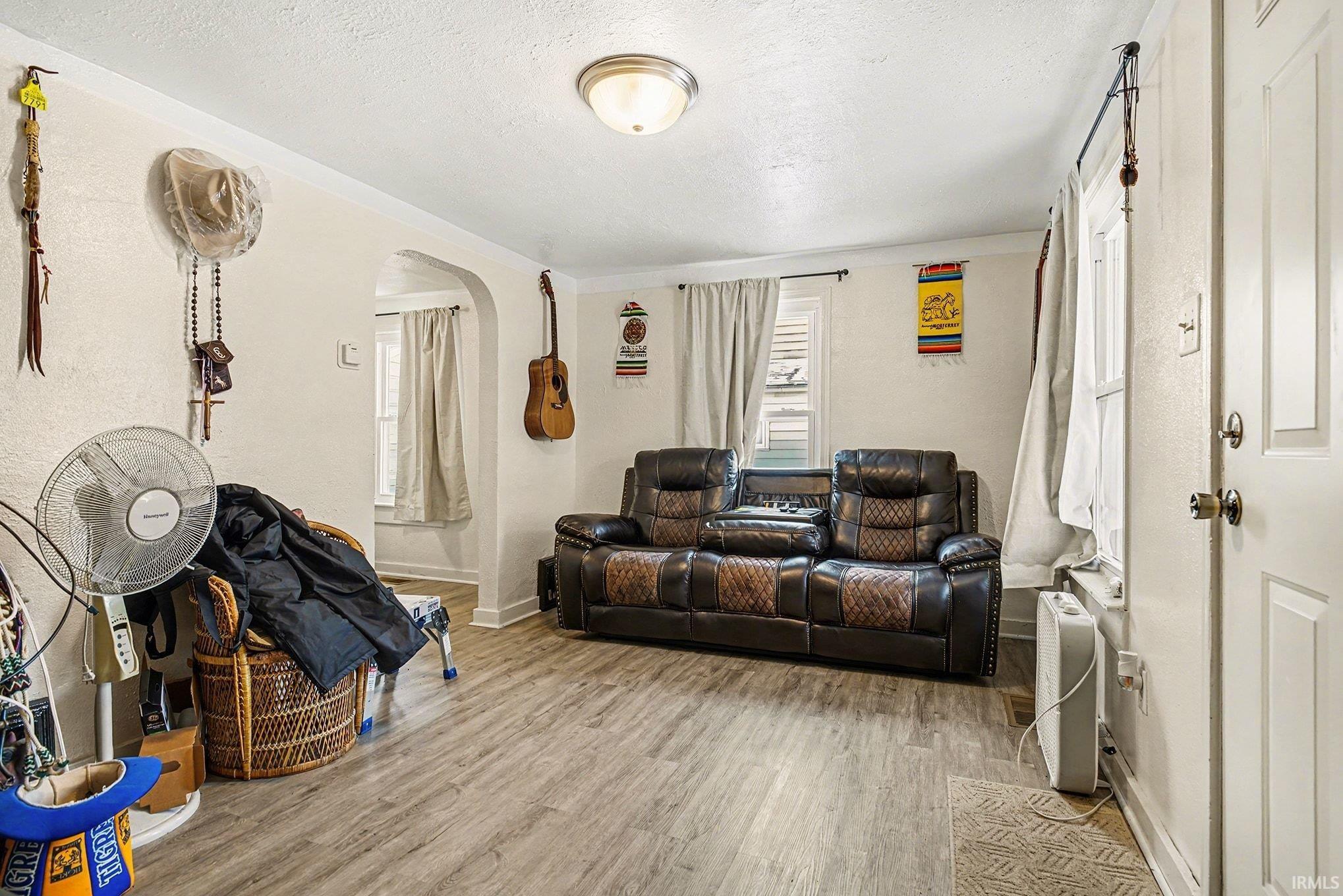 Living area featuring arched walkways, wood finished floors, and a textured ceiling