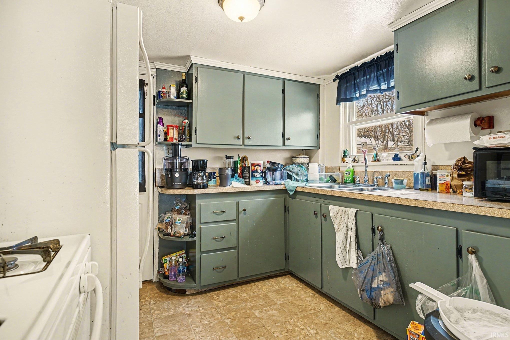 Kitchen with green cabinets, white appliances, light countertops, open shelves, and light floors
