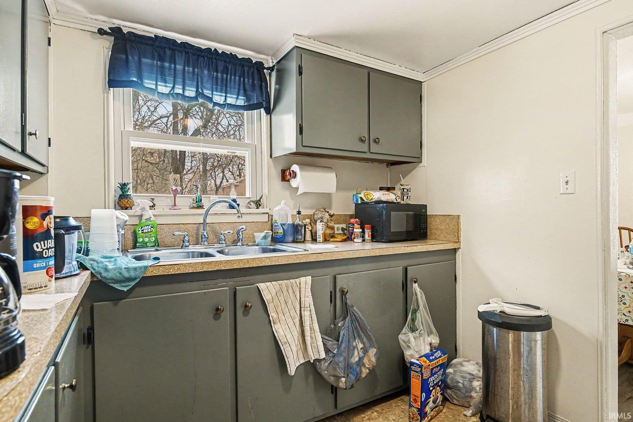 Kitchen featuring crown molding, light countertops, gray cabinetry, and black microwave