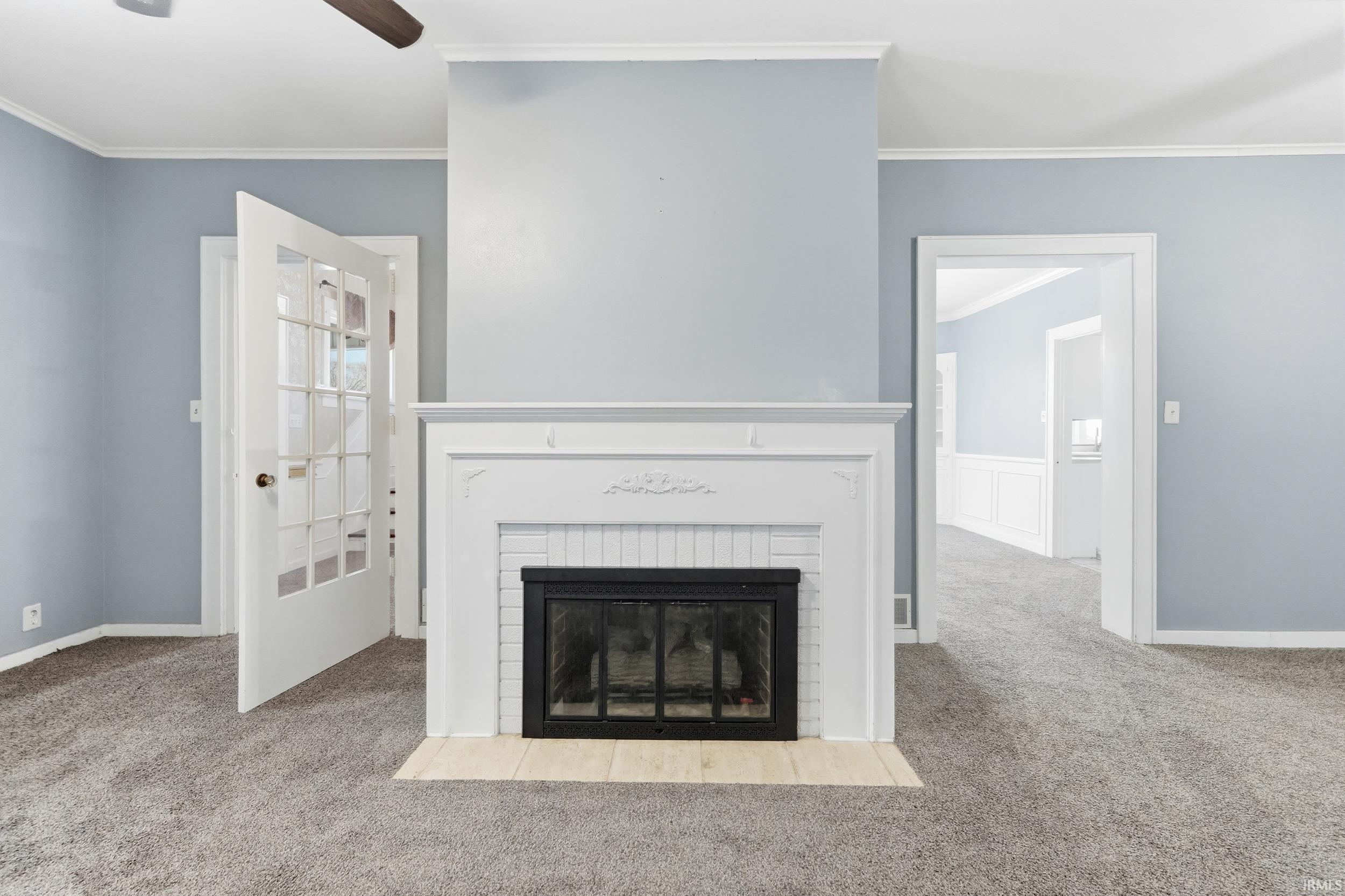 Unfurnished living room with ornamental molding, a brick fireplace, carpet floors, and a ceiling fan
