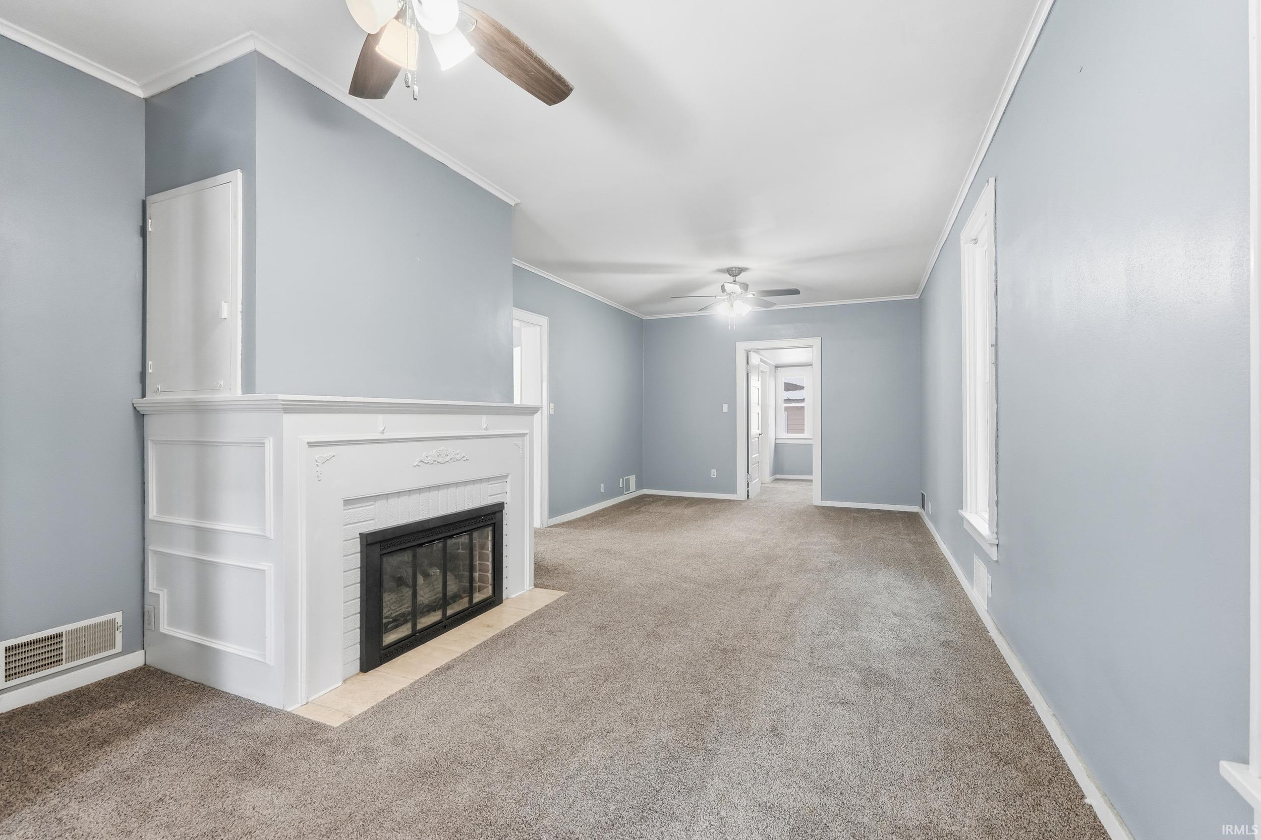 Unfurnished living room with crown molding, carpet, a brick fireplace, and ceiling fan