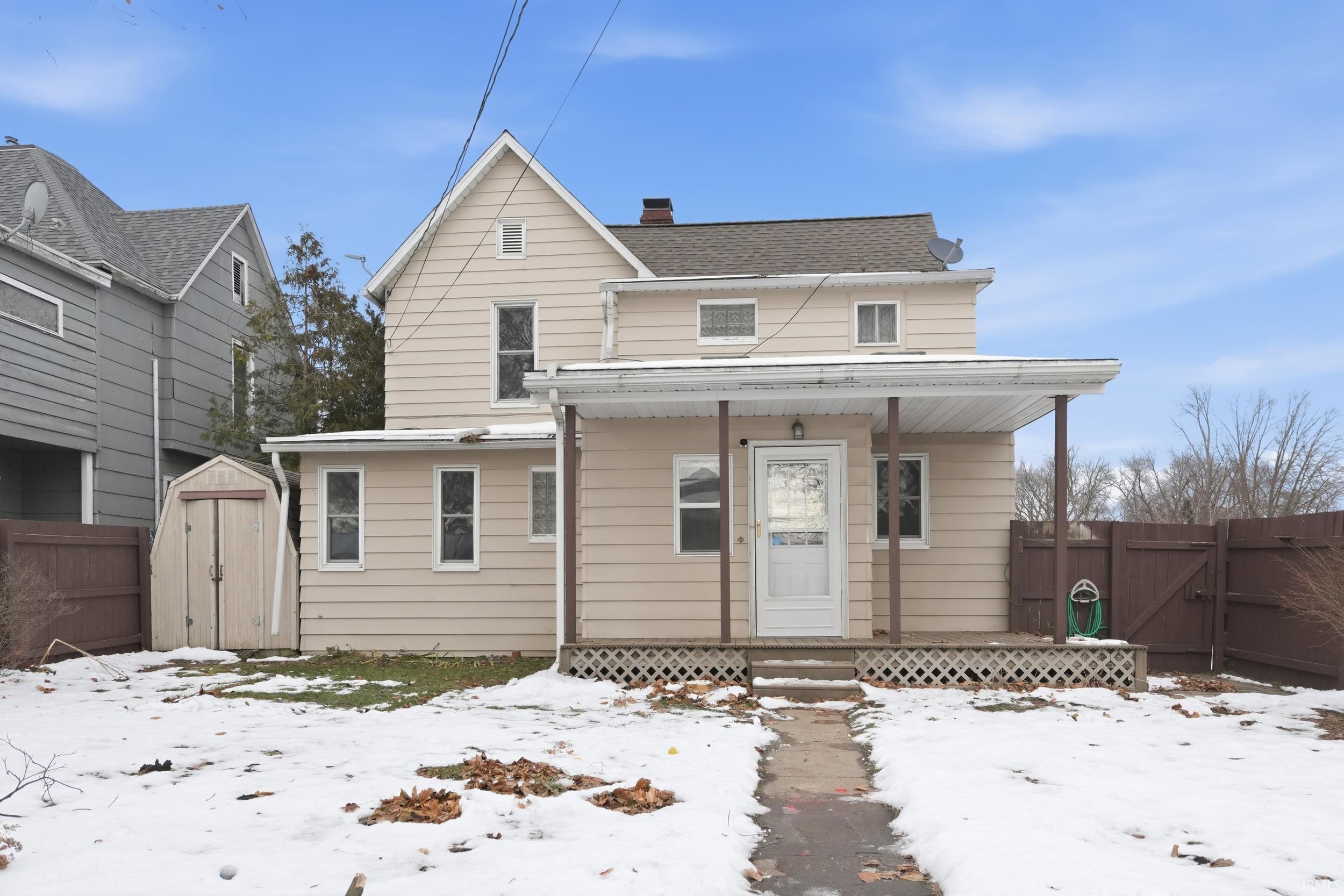 Snow covered back of property with a storage shed, covered porch, a gate, and a chimney