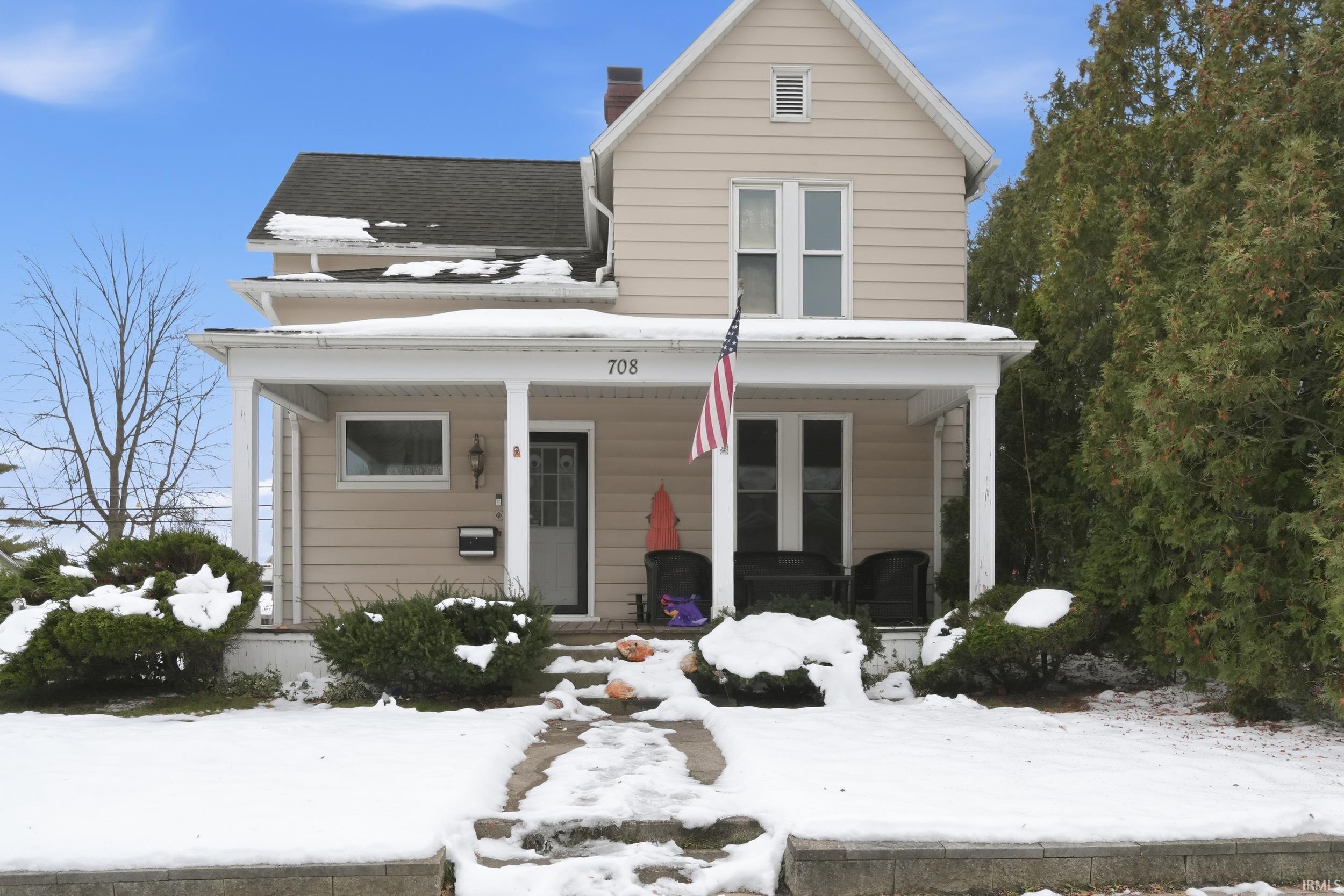 View of front of property with covered porch, a chimney, and a shingled roof