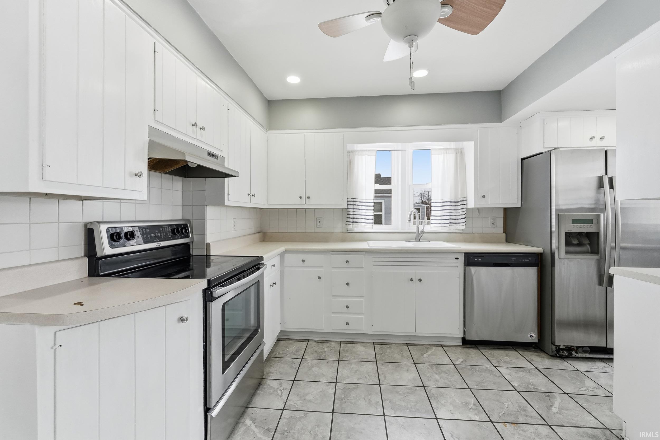 Kitchen with appliances with stainless steel finishes, light countertops, under cabinet range hood, white cabinetry, and a ceiling fan