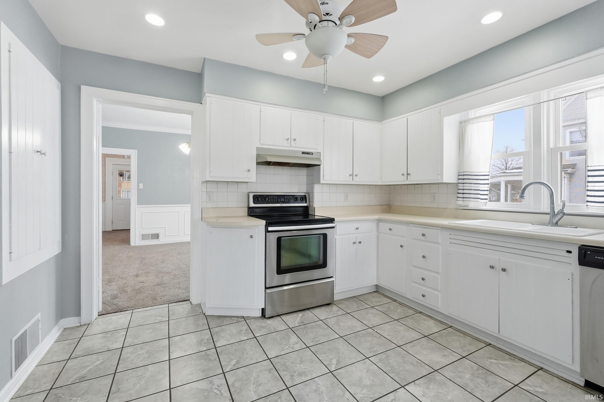 Kitchen featuring stainless steel appliances, light countertops, white cabinetry, a ceiling fan, and a wainscoted wall