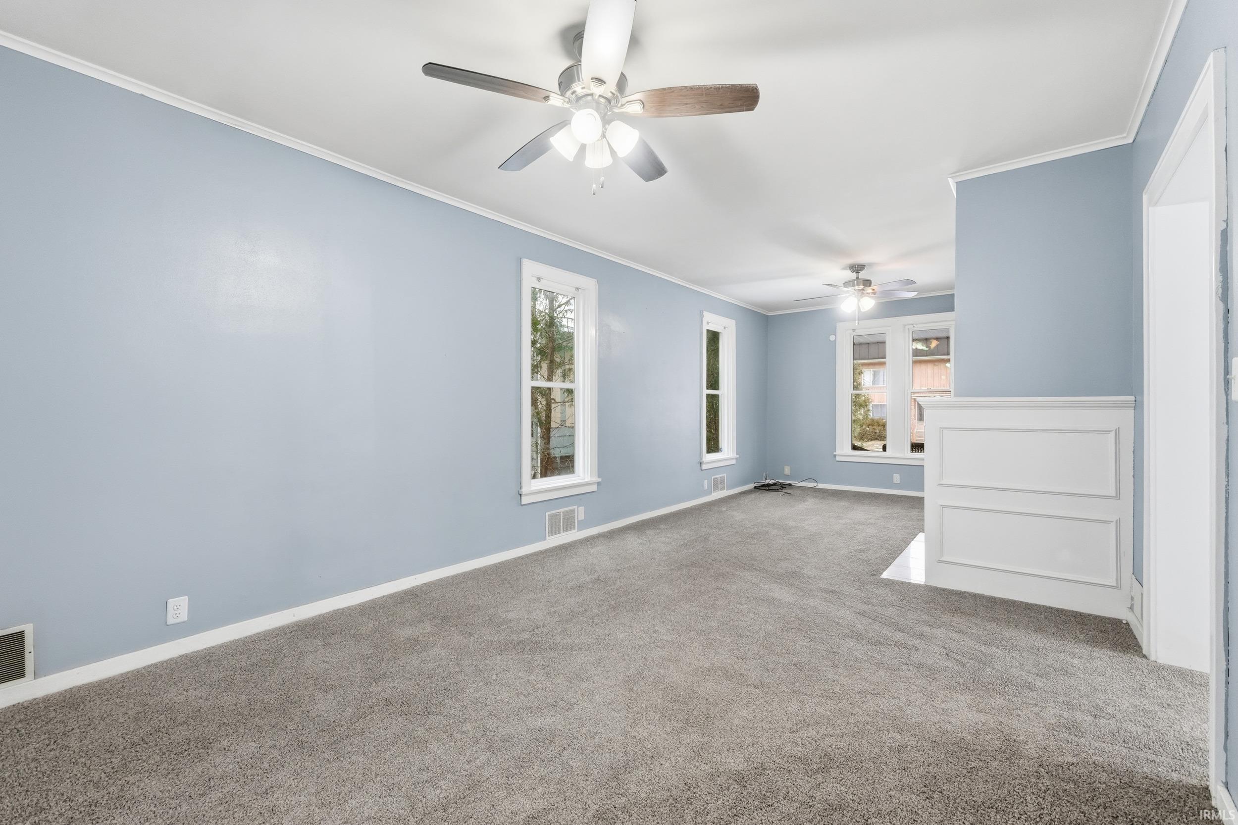 Carpeted spare room featuring plenty of natural light, crown molding, and ceiling fan