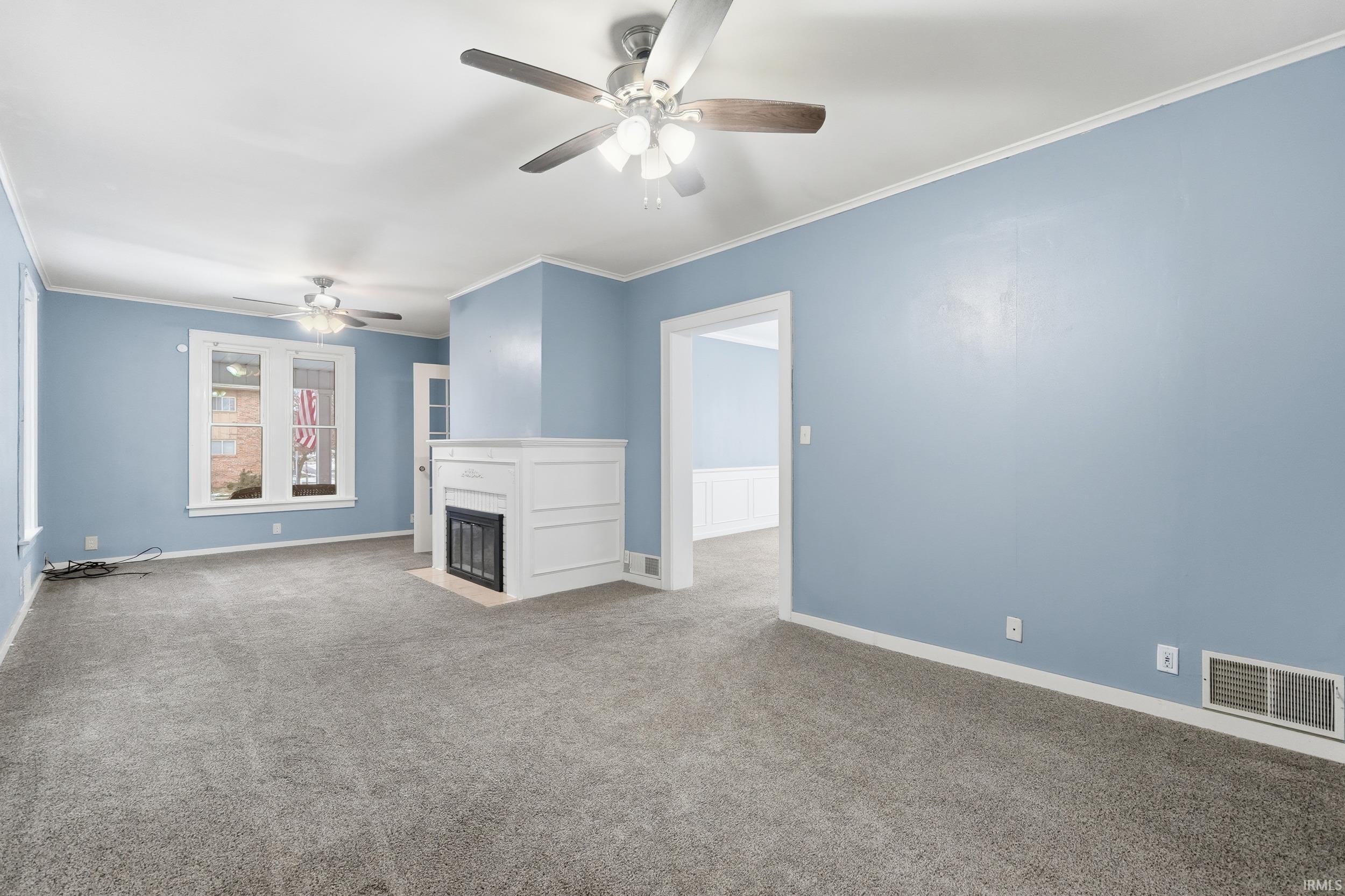 Unfurnished living room with a fireplace with flush hearth, crown molding, carpet, and ceiling fan