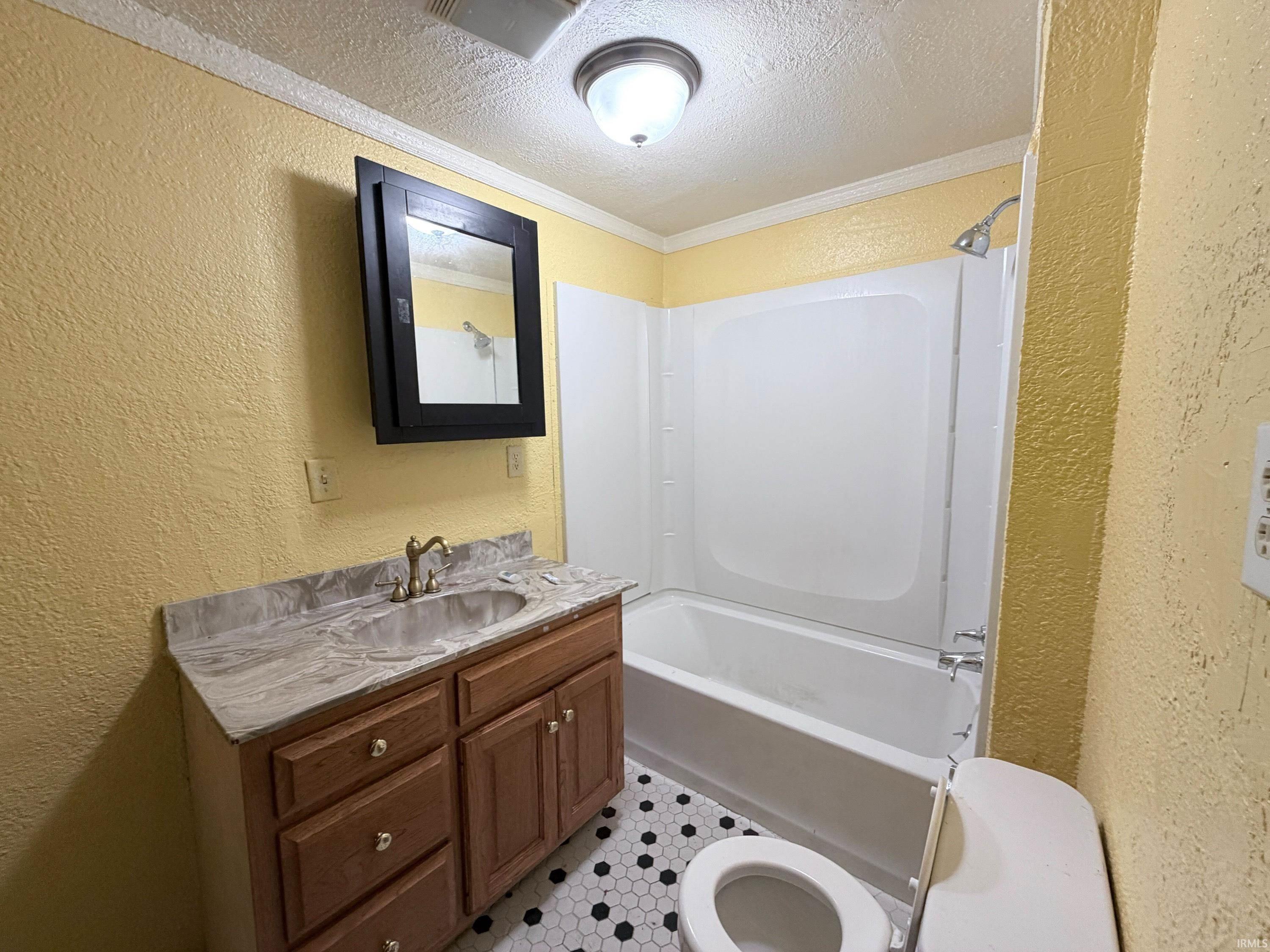 Bathroom featuring a textured wall, a textured ceiling, vanity, and washtub / shower combination