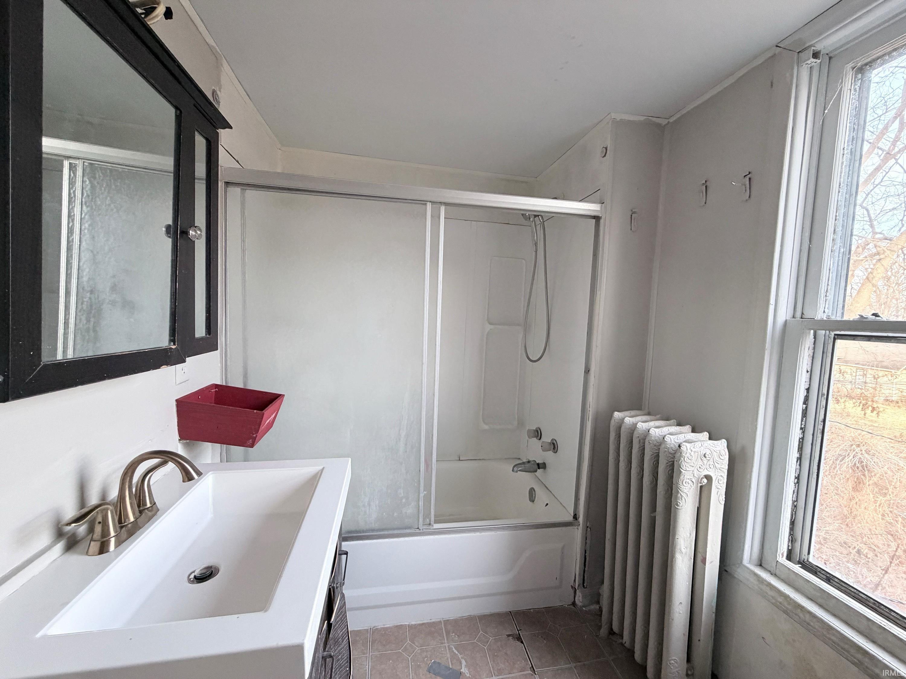 Bathroom featuring radiator heating unit, combined bath / shower with glass door, vanity, and light tile patterned floors