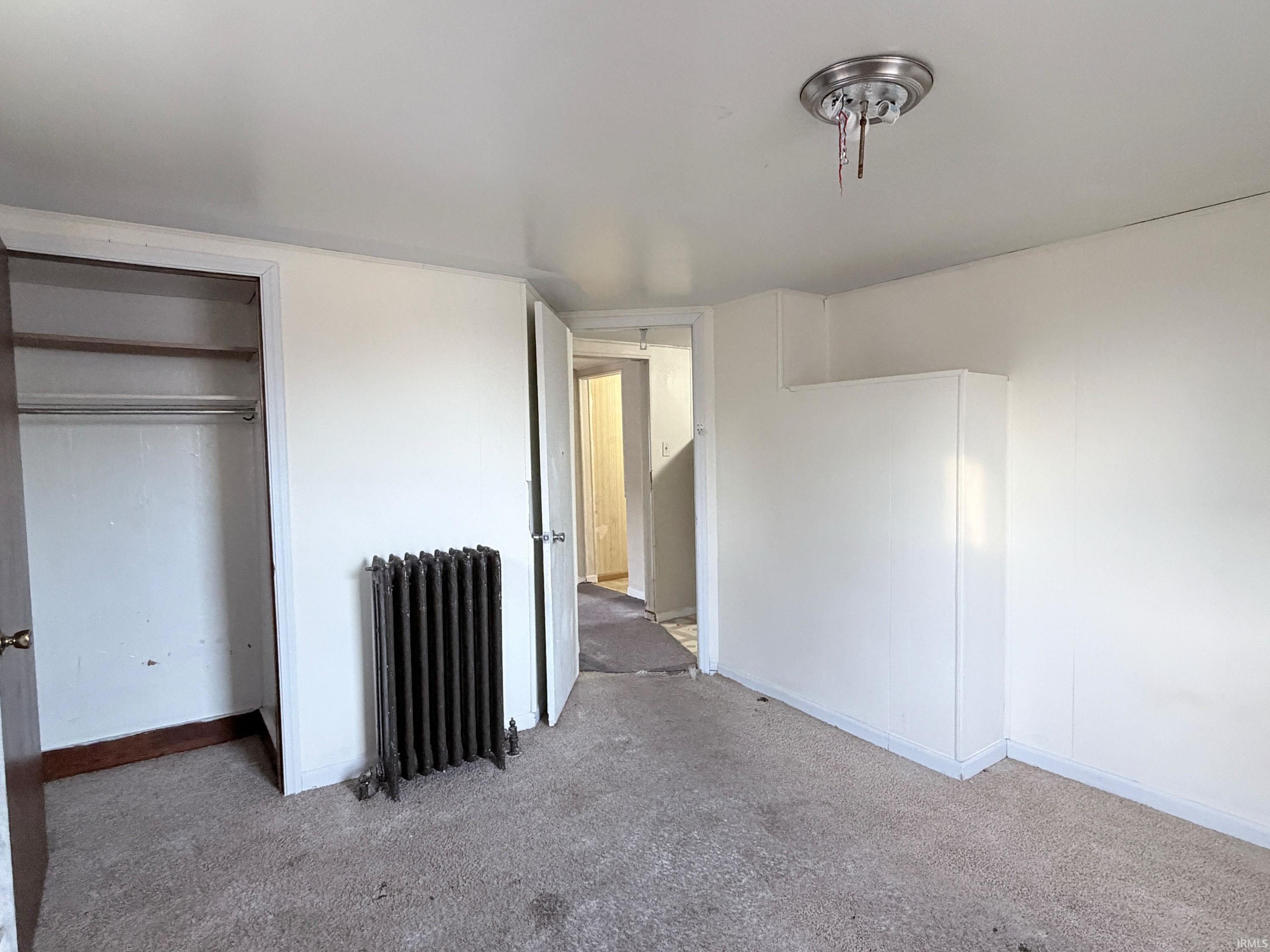Unfurnished bedroom featuring radiator, a closet, and carpet floors