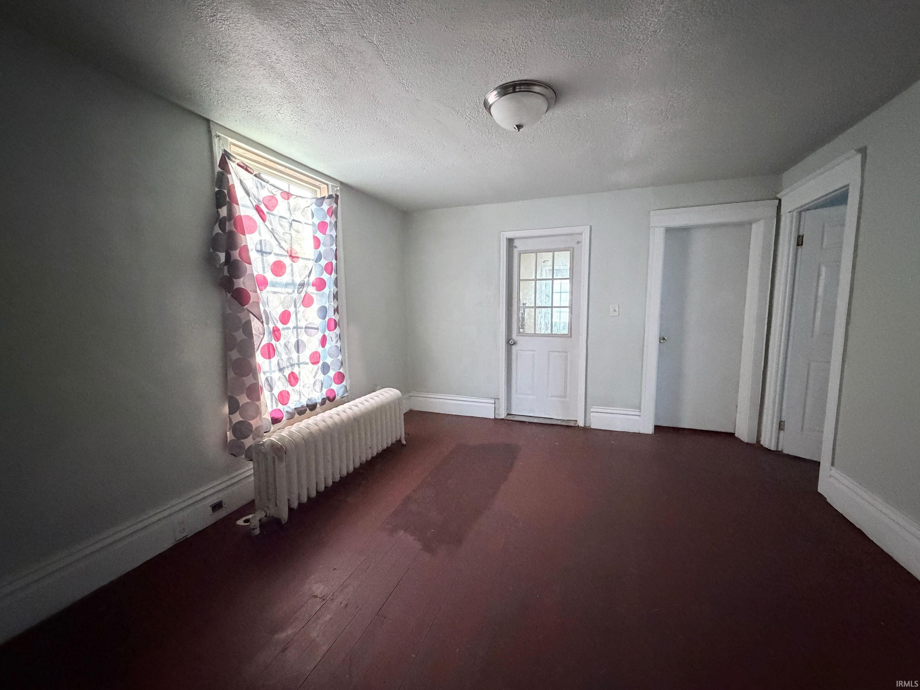 Spare room featuring a textured ceiling, radiator, and dark wood finished floors