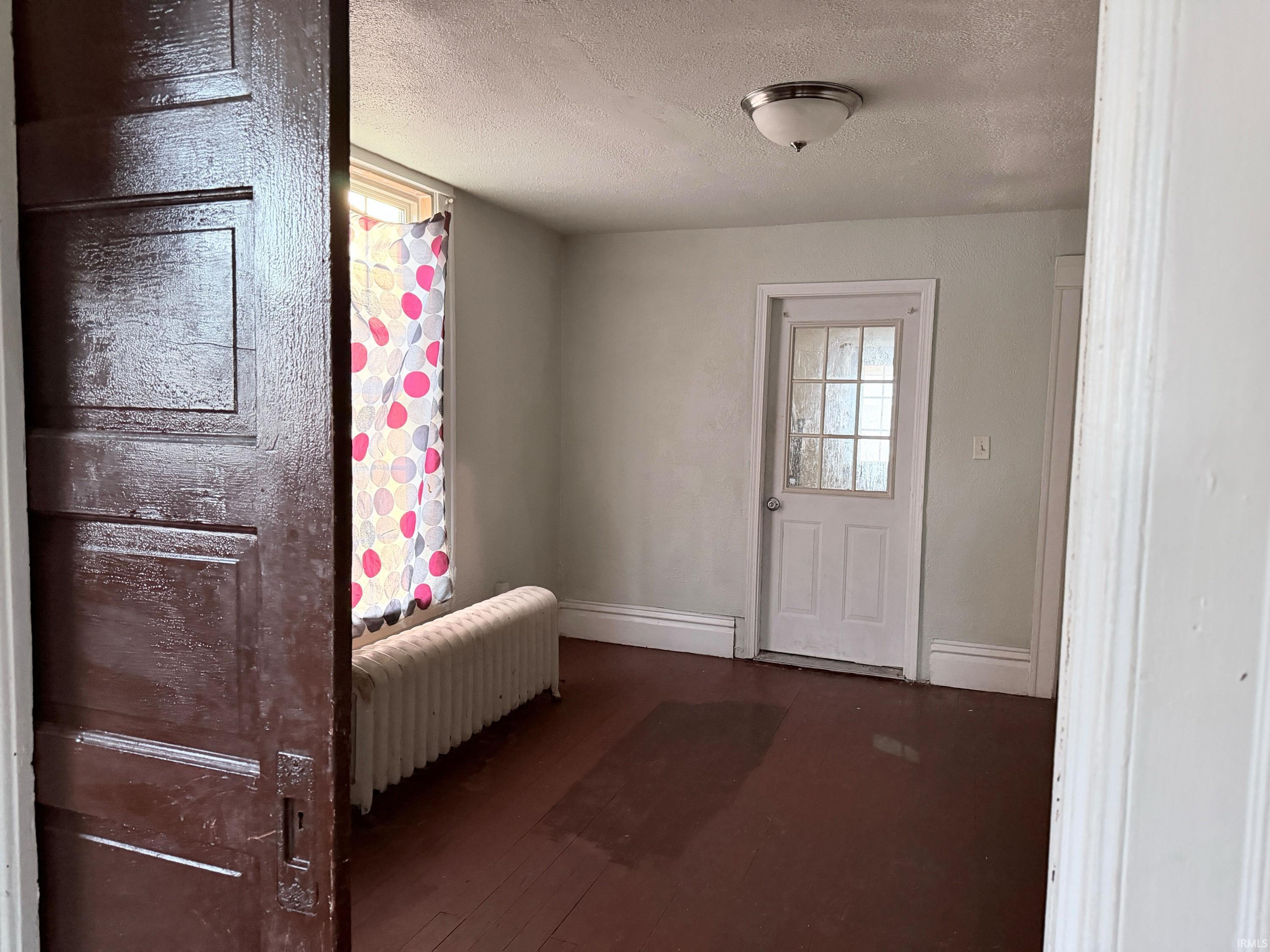 Entryway with radiator heating unit, a textured ceiling, and hardwood / wood-style floors