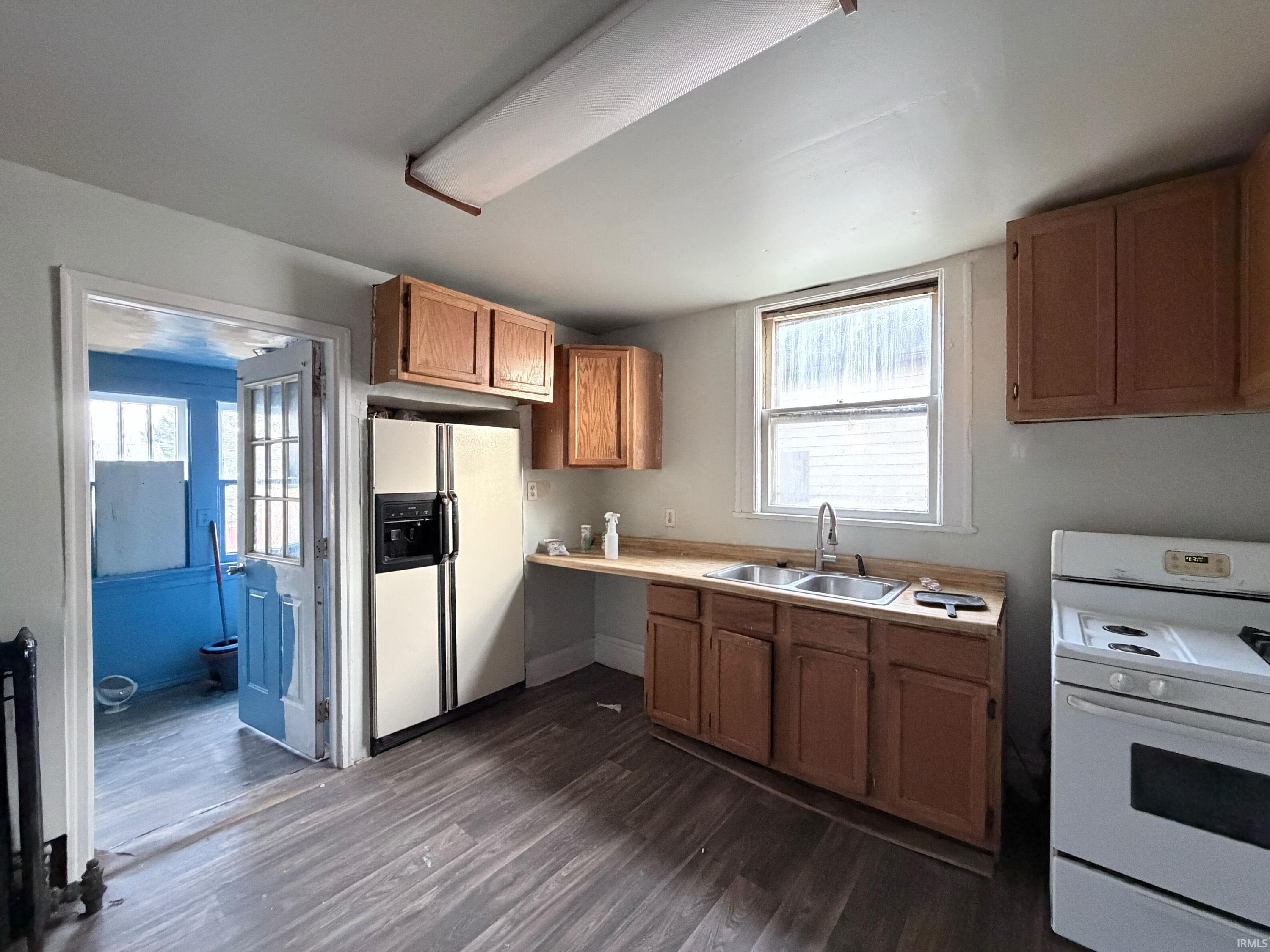 Kitchen with white appliances, light countertops, dark wood finished floors, brown cabinets, and healthy amount of natural light