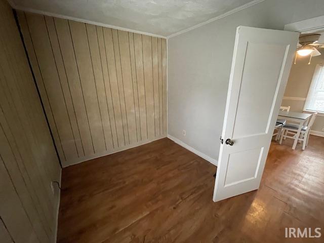 Spare room featuring wood walls, dark wood-style floors, ornamental molding, and ceiling fan