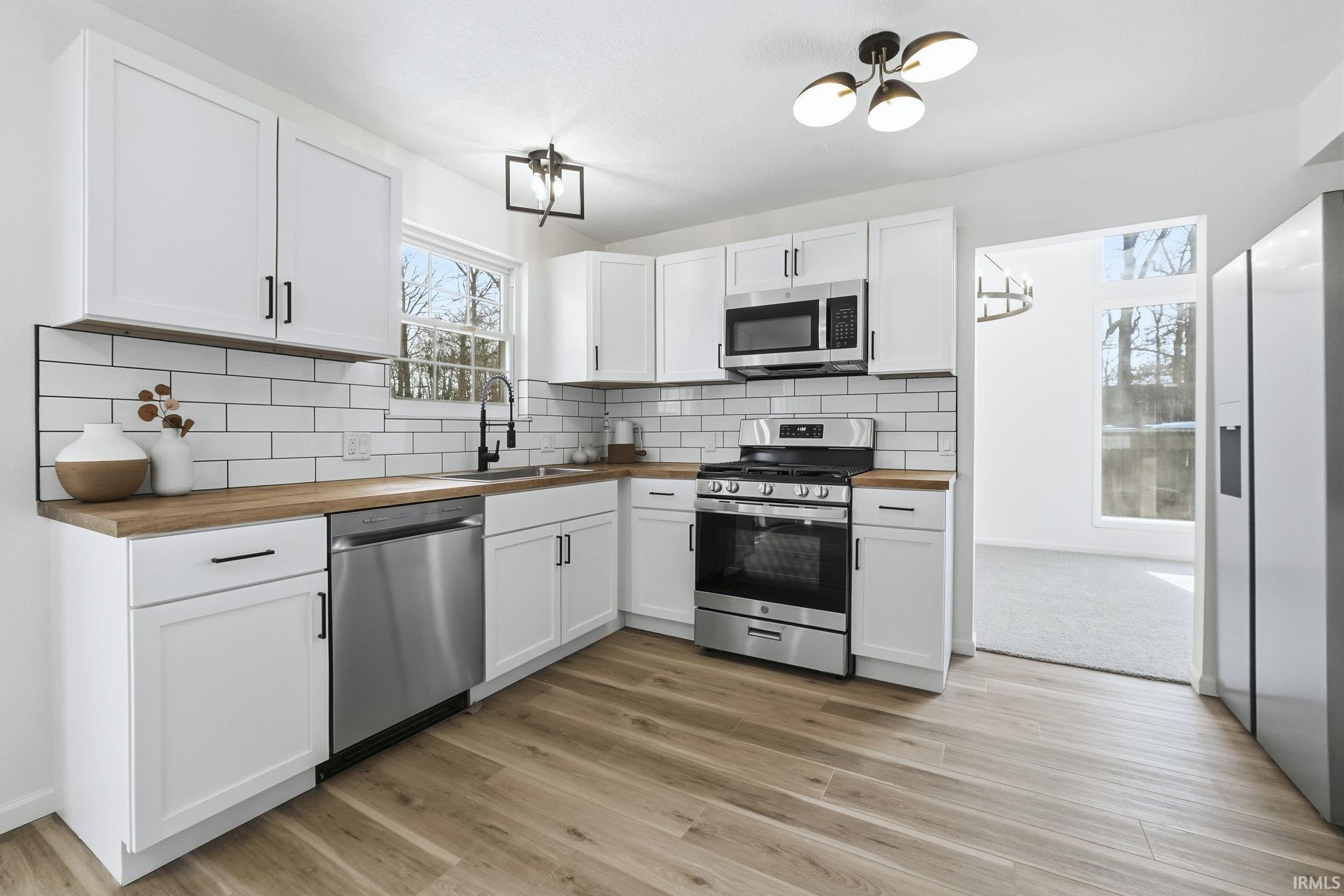 Kitchen featuring butcher block counters, stainless steel appliances, white cabinets, and luxury vinyl plank flooring