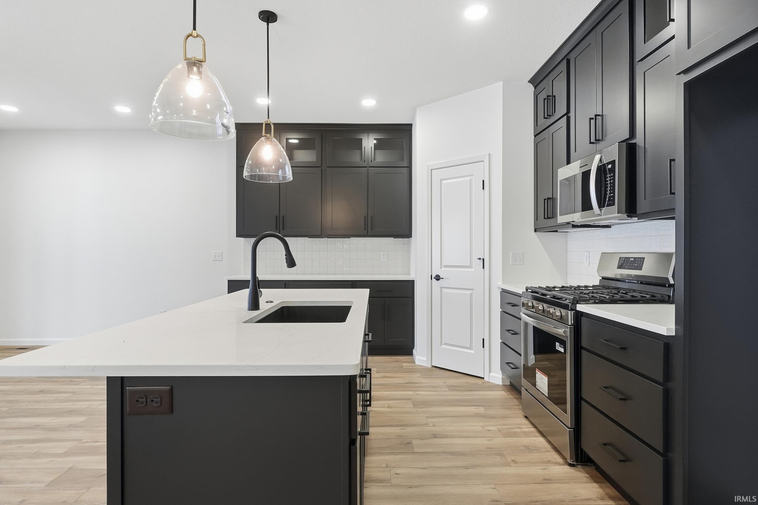Kitchen featuring stainless steel appliances, pendant lighting, light stone countertops, light wood finished floors, and an island with sink