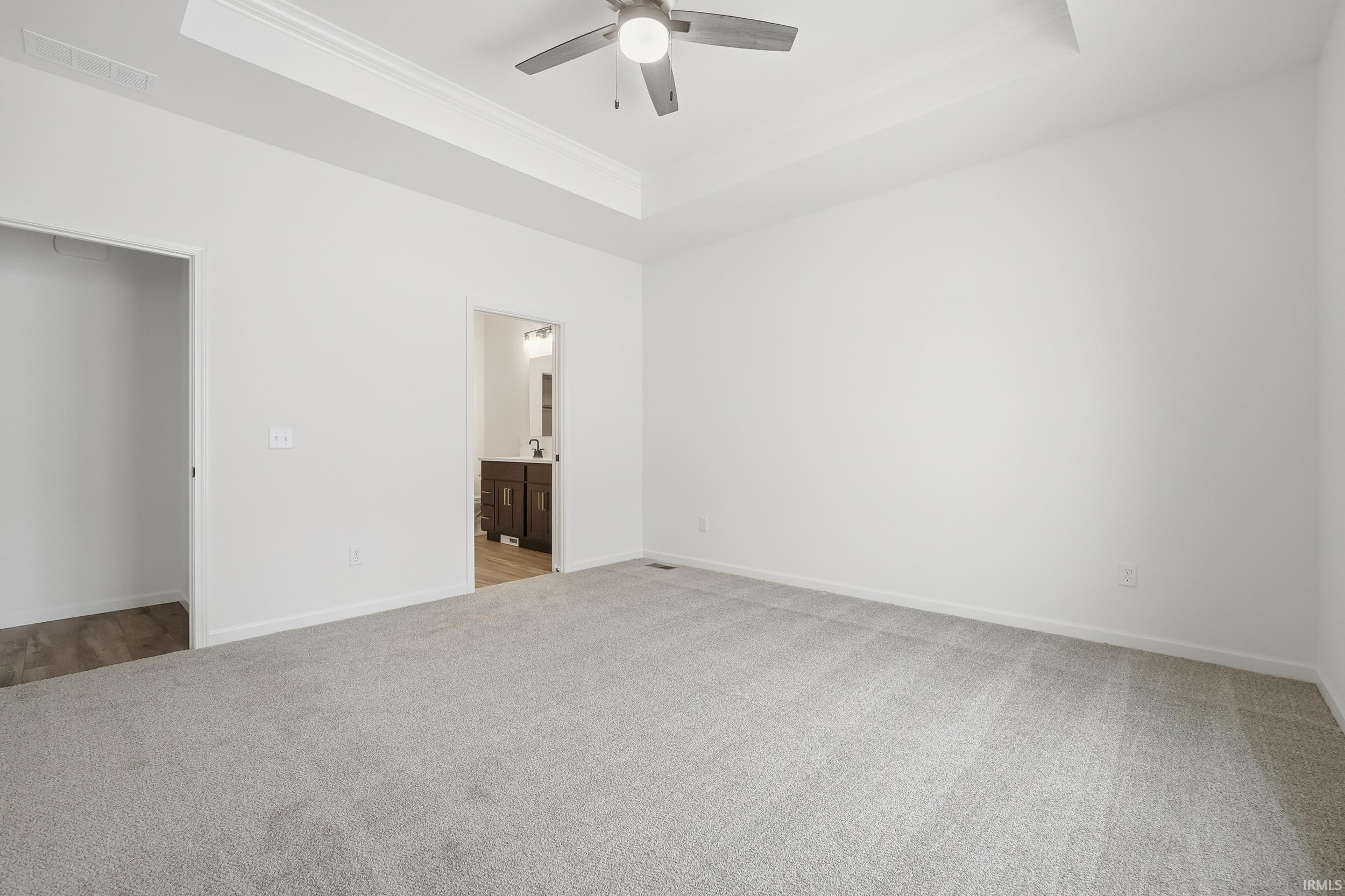 Unfurnished bedroom featuring a tray ceiling, light colored carpet, ceiling fan, and ensuite bathroom