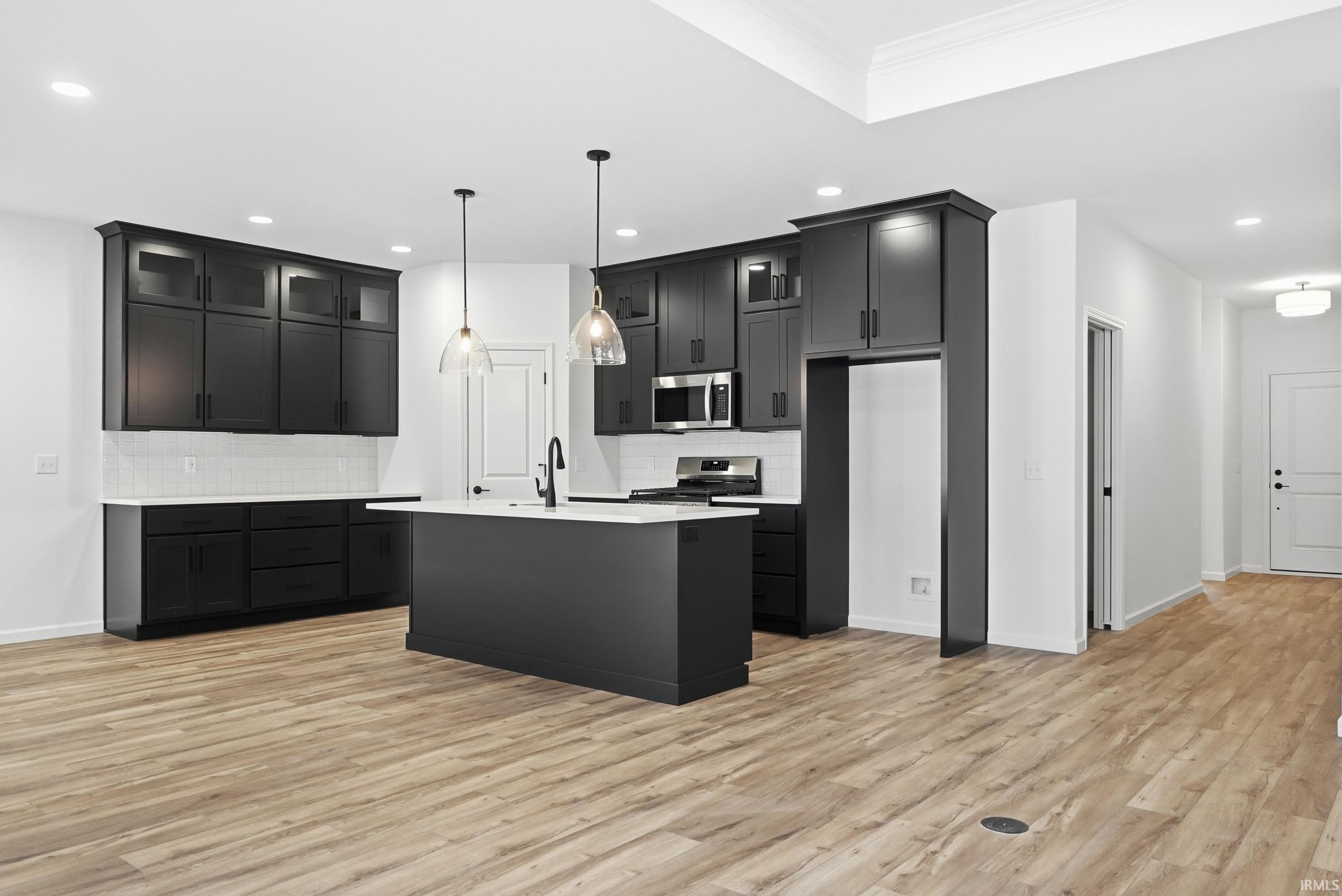 Kitchen with glass insert cabinets, a center island with sink, dark cabinetry, decorative light fixtures, and recessed lighting