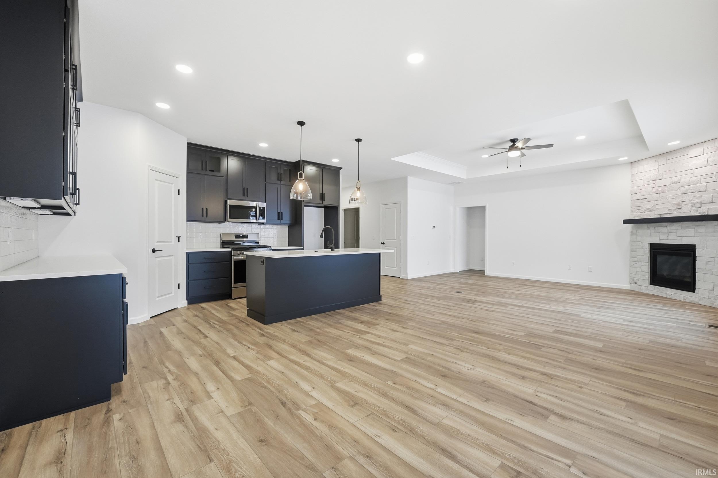 Kitchen featuring open floor plan, decorative light fixtures, dark cabinets, a kitchen island with sink, and light wood-style flooring