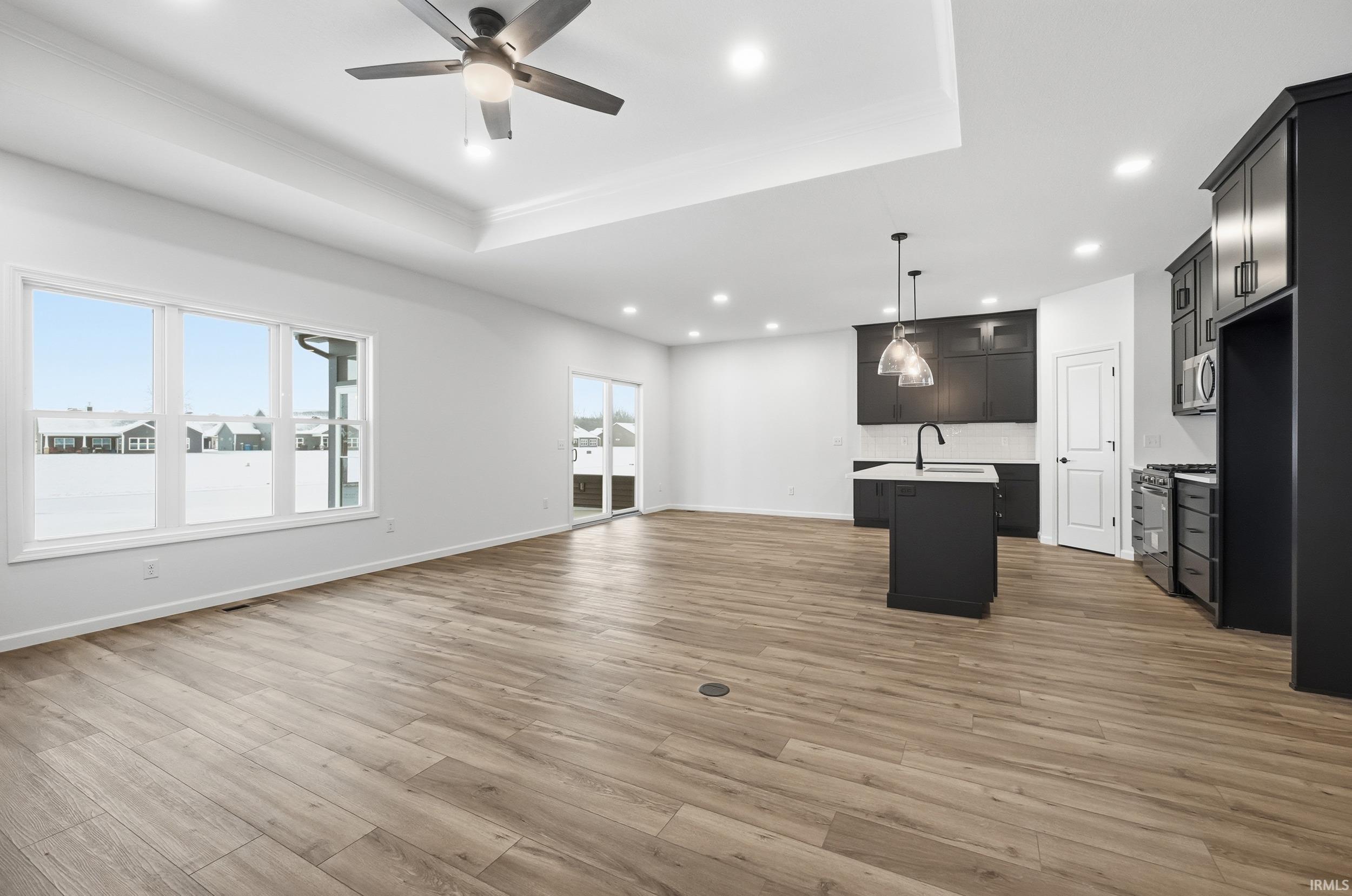 Unfurnished living room with light wood-style flooring, a ceiling fan, recessed lighting, a tray ceiling, and ornamental molding