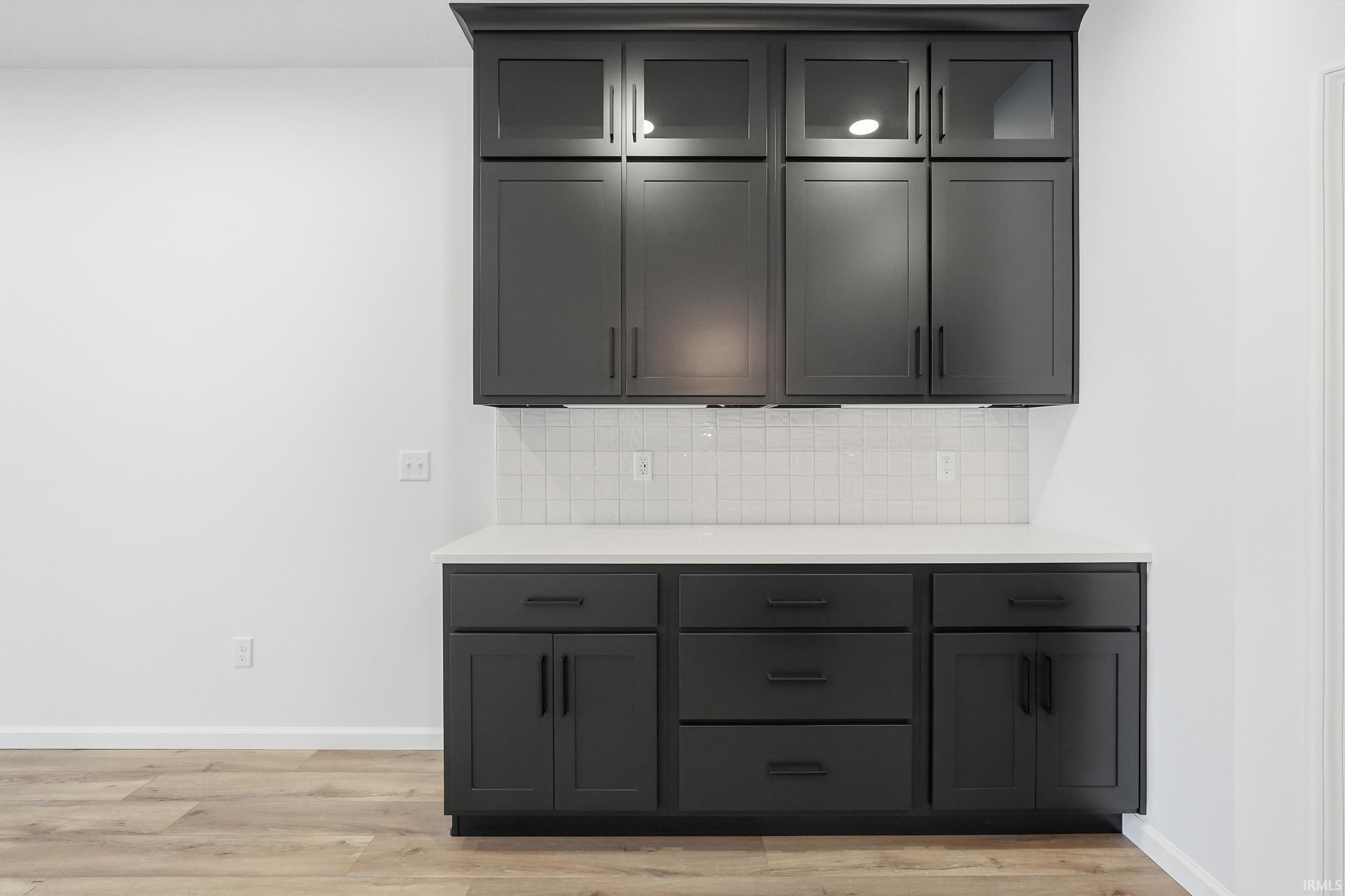 Kitchen featuring decorative backsplash, light wood-style flooring, glass insert cabinets, and light stone counters