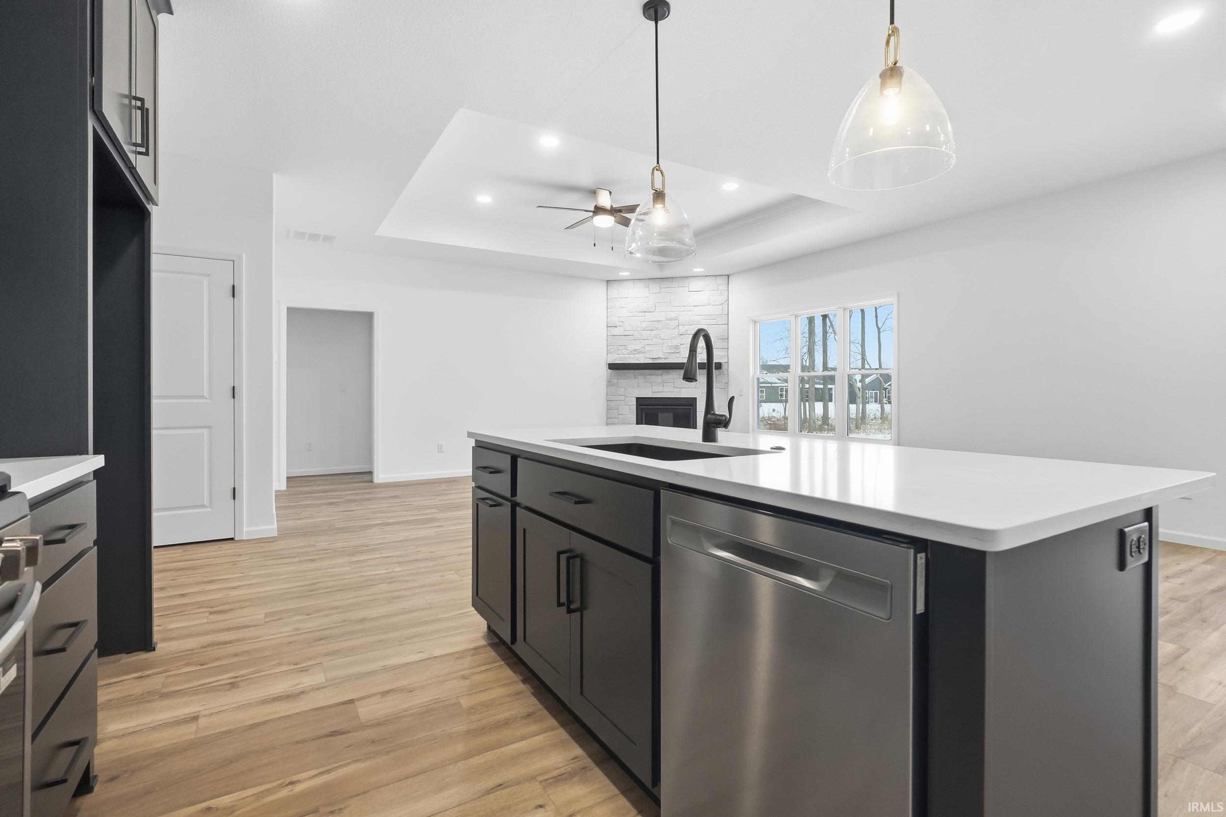 Kitchen with an island with sink, dishwasher, hanging light fixtures, dark cabinetry, and recessed lighting