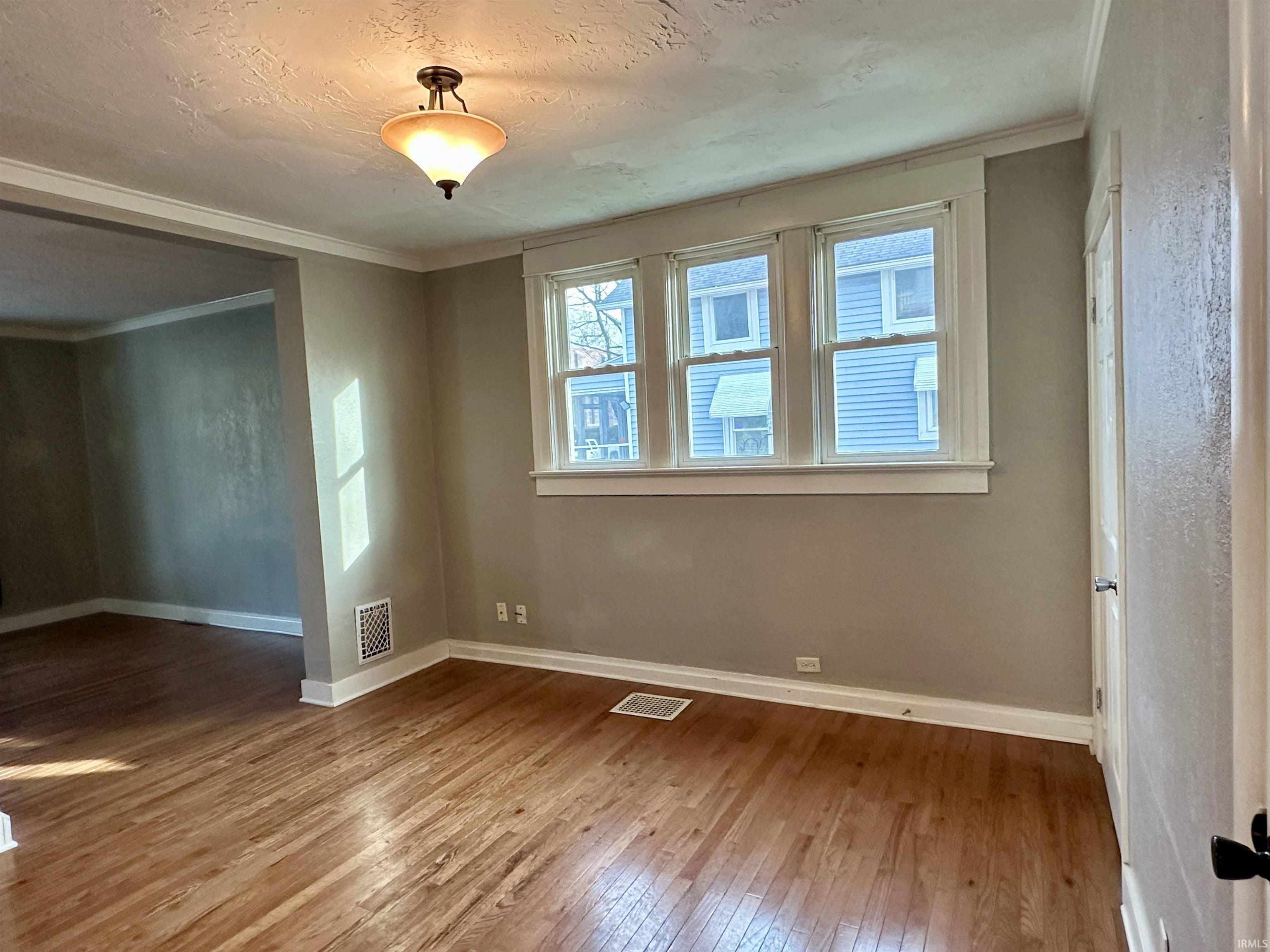 Spare room featuring wood-type flooring, crown molding, and a textured ceiling