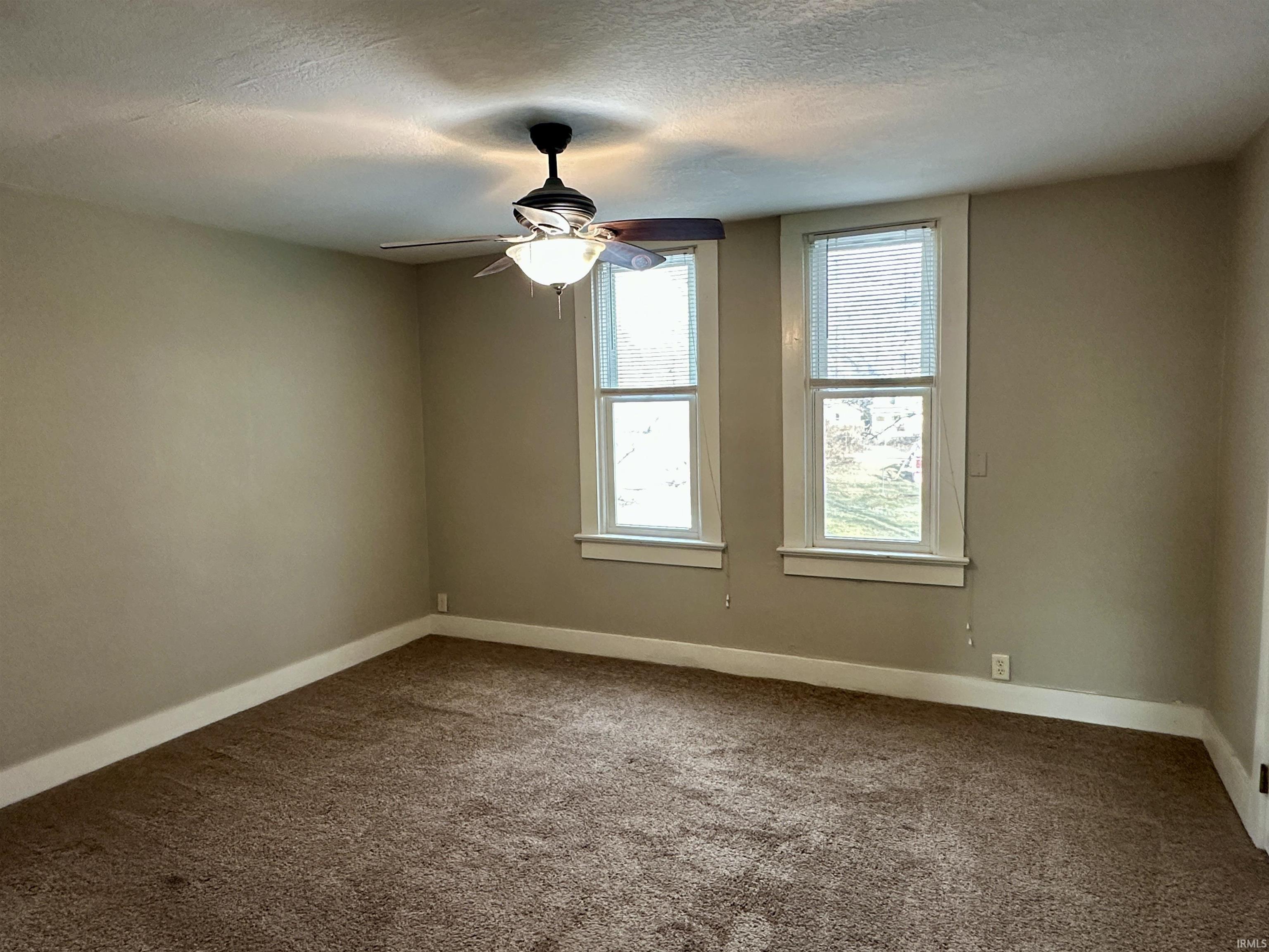 Carpeted empty room with a textured ceiling and a ceiling fan