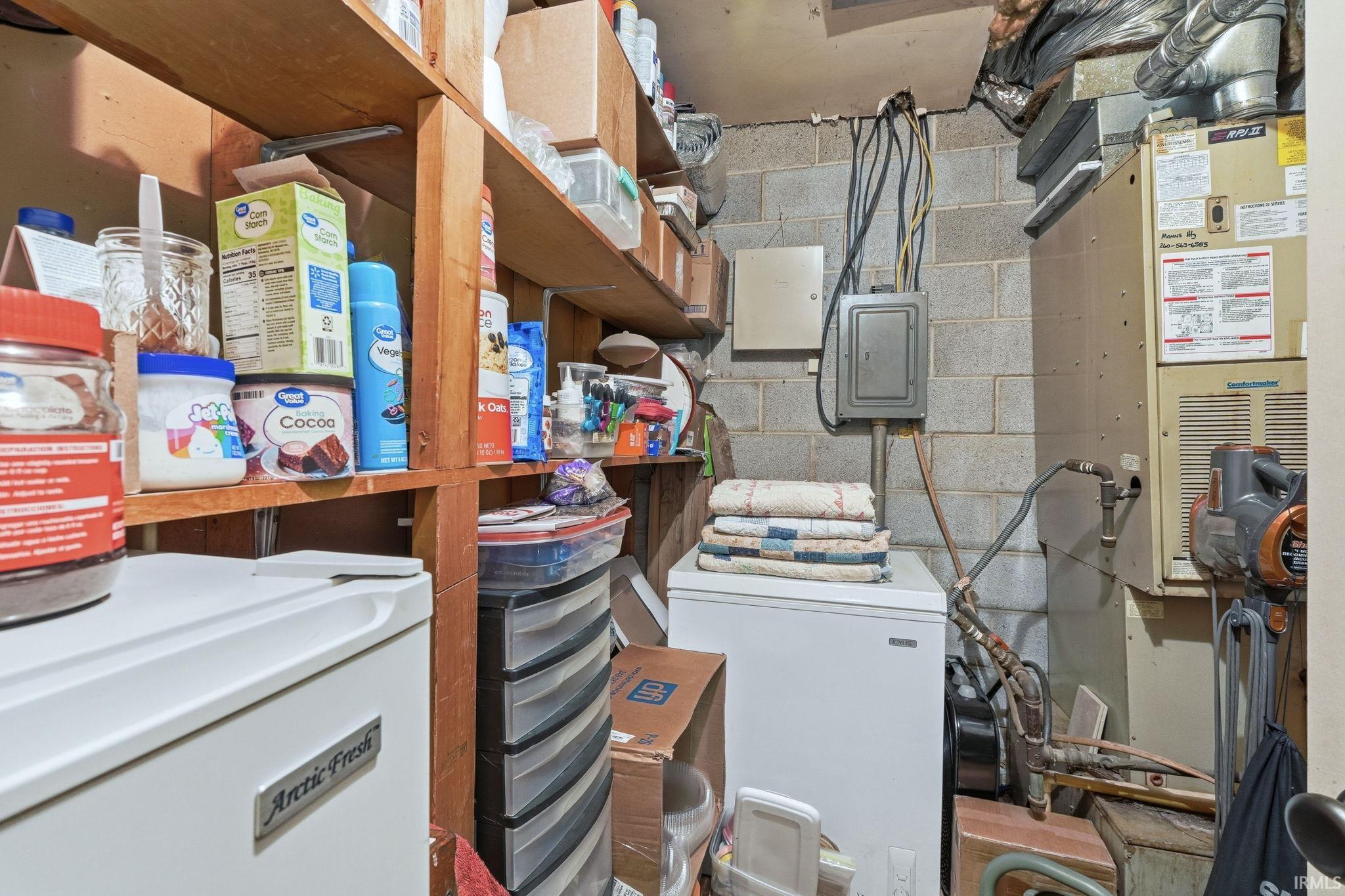 Unfinished below grade area with washer / clothes dryer, heating unit, electric panel, and white refrigerator