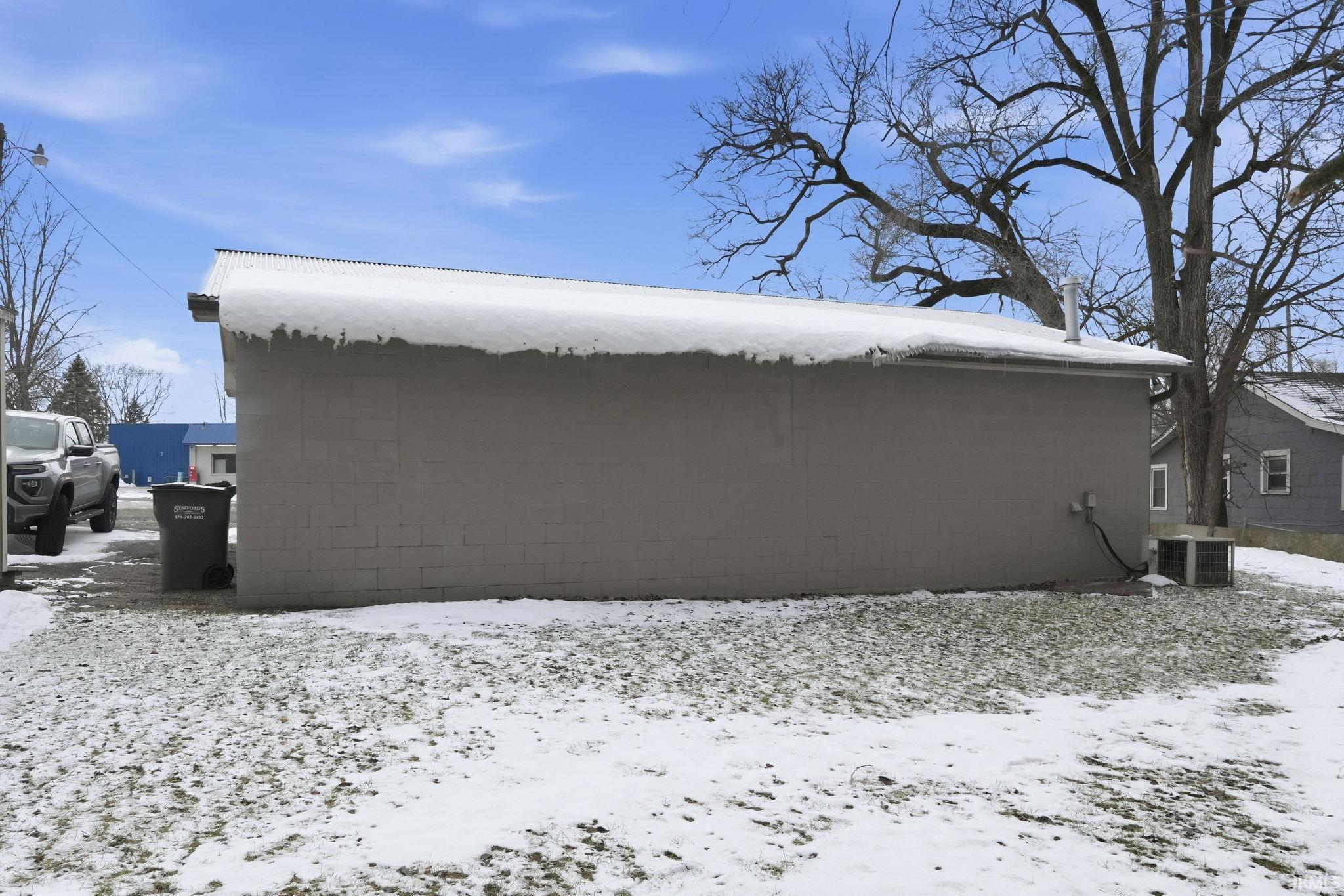 View of snow covered exterior with concrete block siding and a central air condition unit