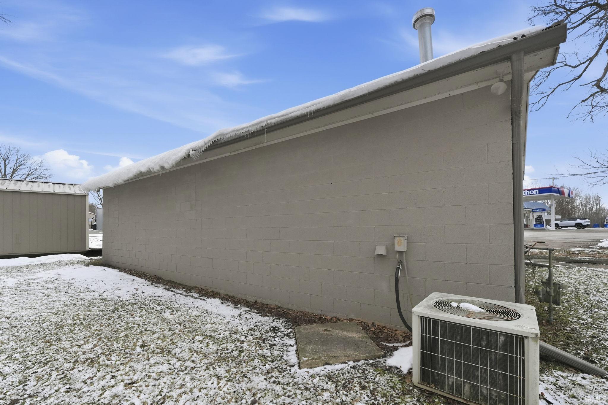 View of snowy exterior with concrete block siding and a central AC unit