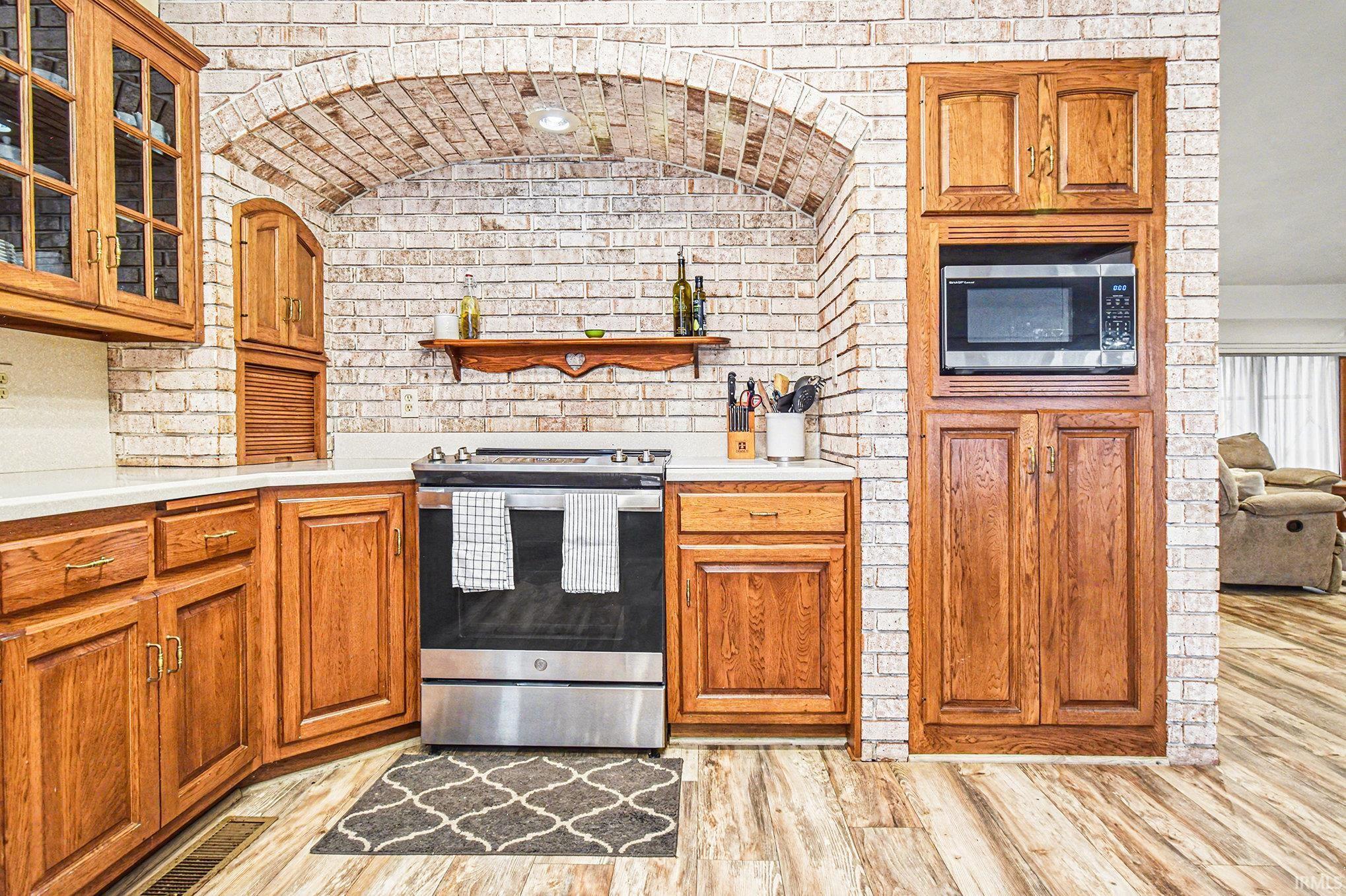 Kitchen featuring appliances with stainless steel finishes, brown cabinets, light countertops, brick wall, and light wood-style floors