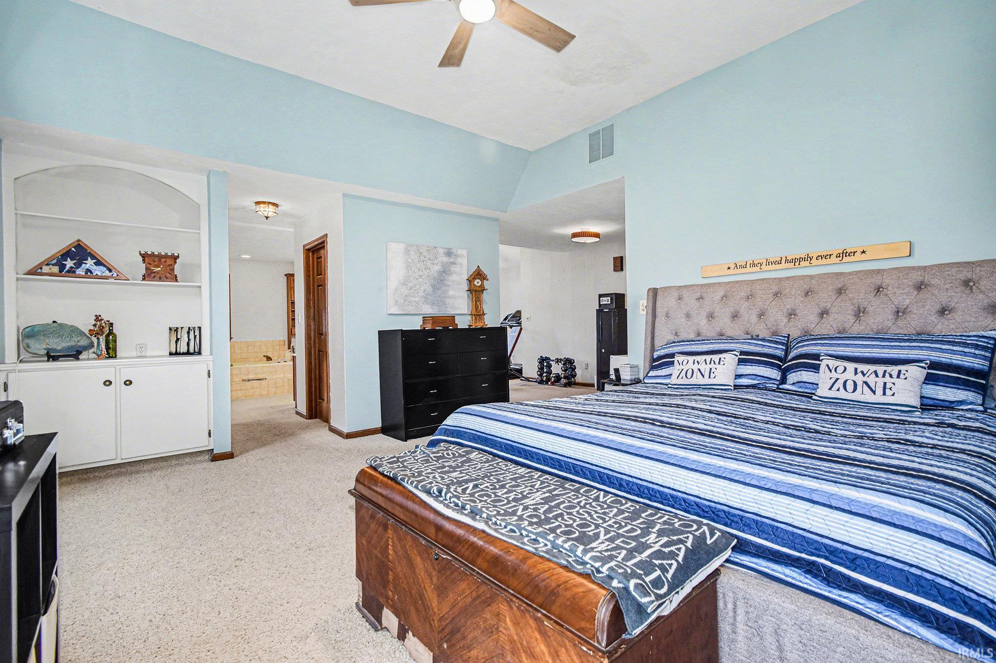 Bedroom with lofted ceiling, light carpet, connected bathroom, and ceiling fan
