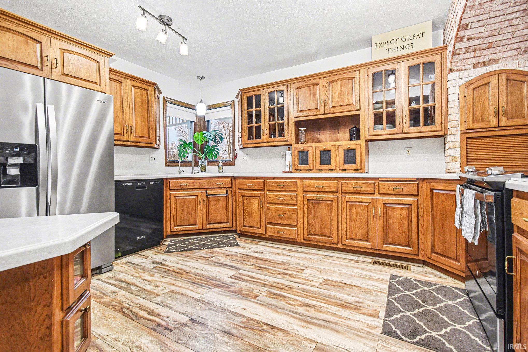 Kitchen featuring black appliances, light countertops, glass insert cabinets, and light wood finished floors