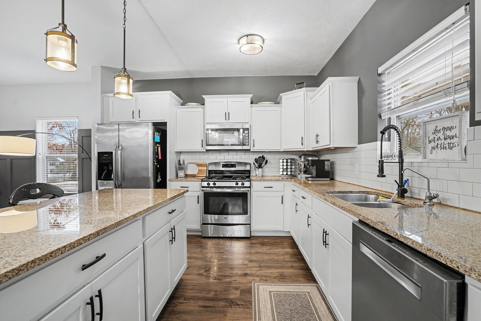 Kitchen featuring appliances with stainless steel finishes, dark wood-type flooring, light stone counters, pendant lighting, and white cabinets