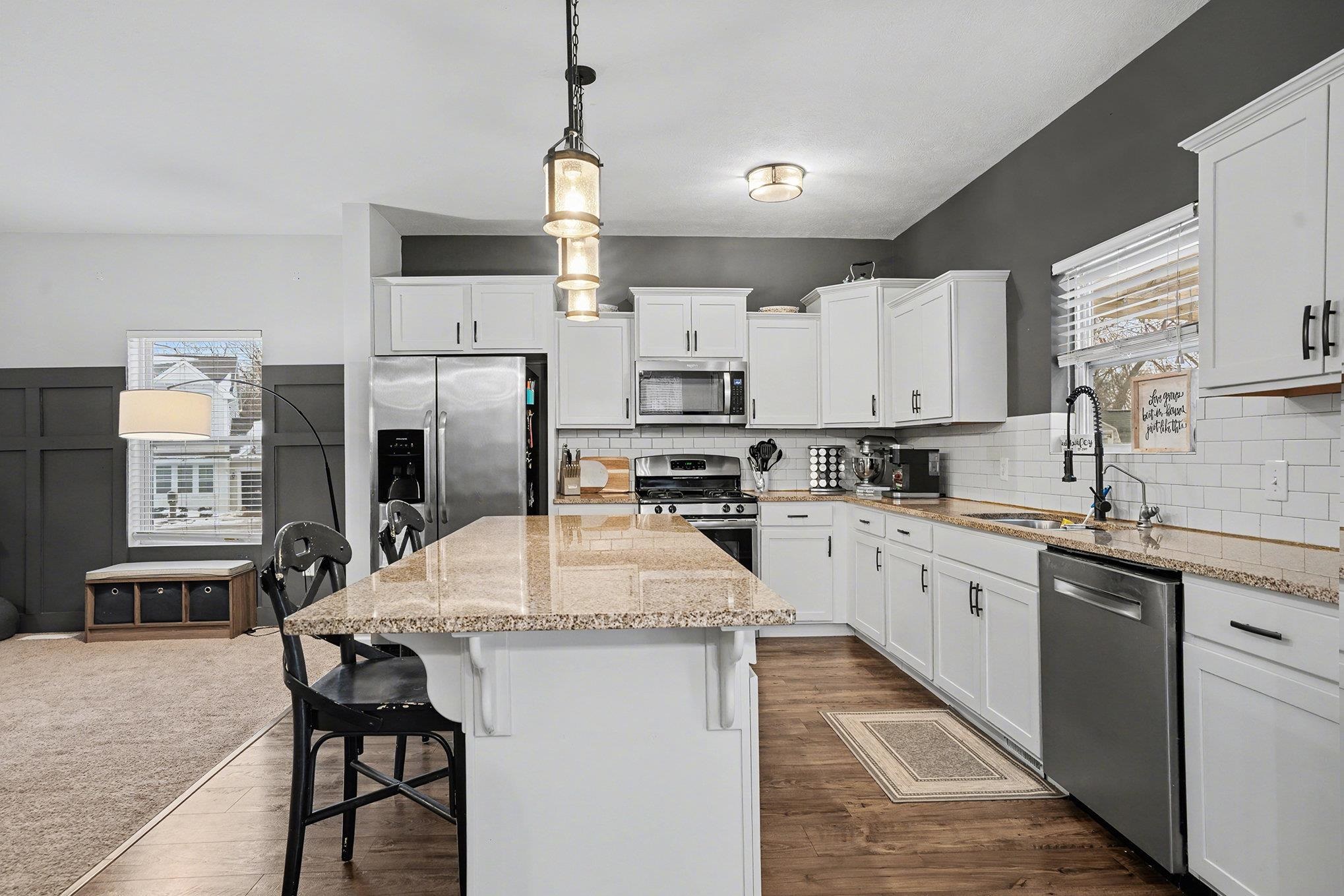 Kitchen featuring a breakfast bar area, decorative light fixtures, appliances with stainless steel finishes, and light stone counters