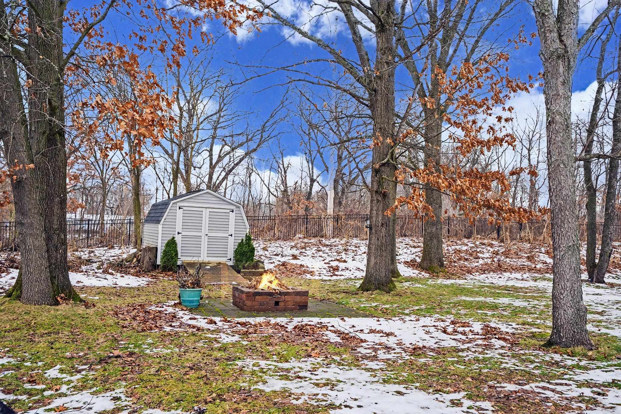 Yard covered in snow featuring an outdoor fire pit and a storage unit