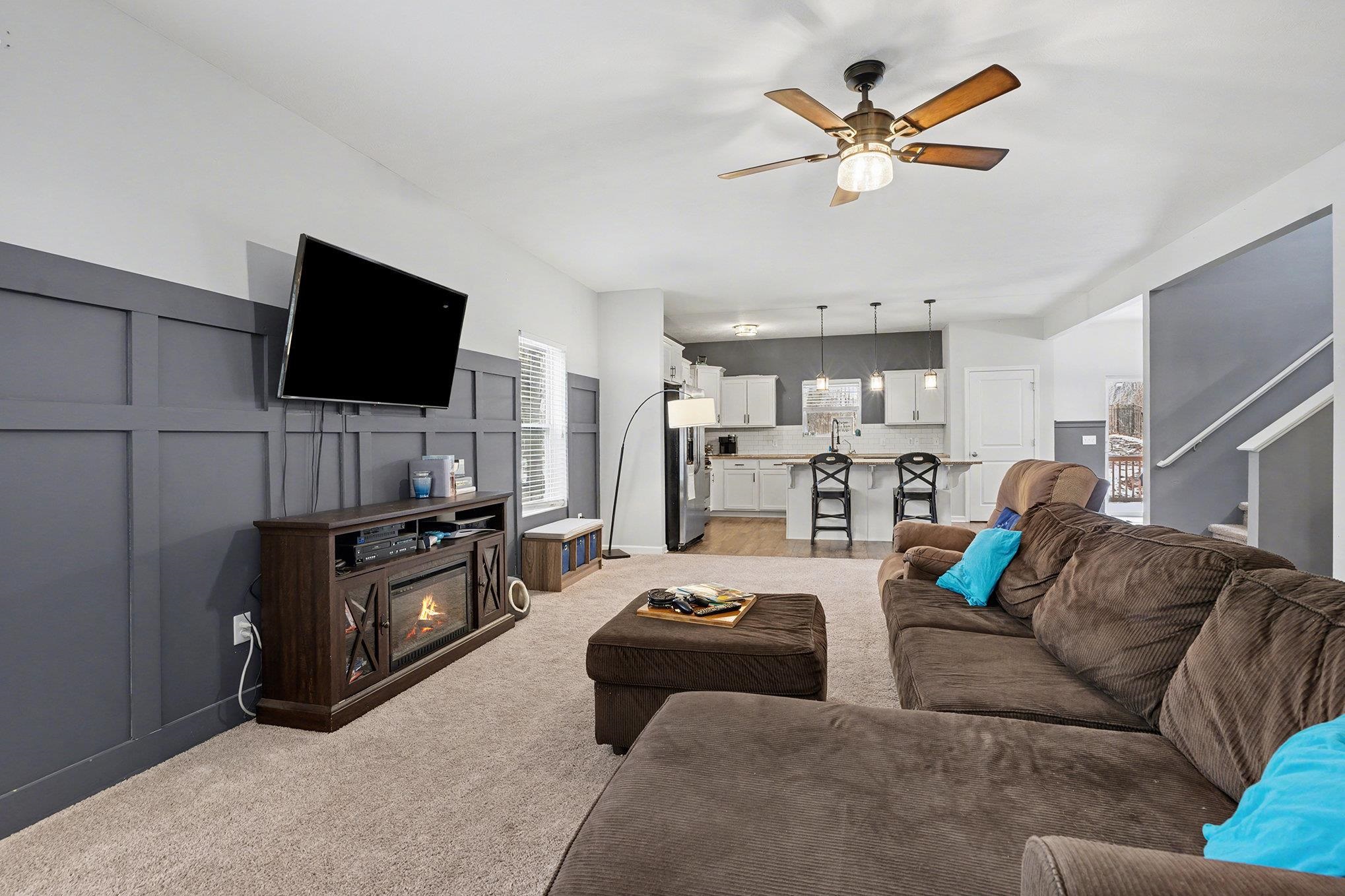Living room with a decorative wall, stairway, ceiling fan, and light colored carpet