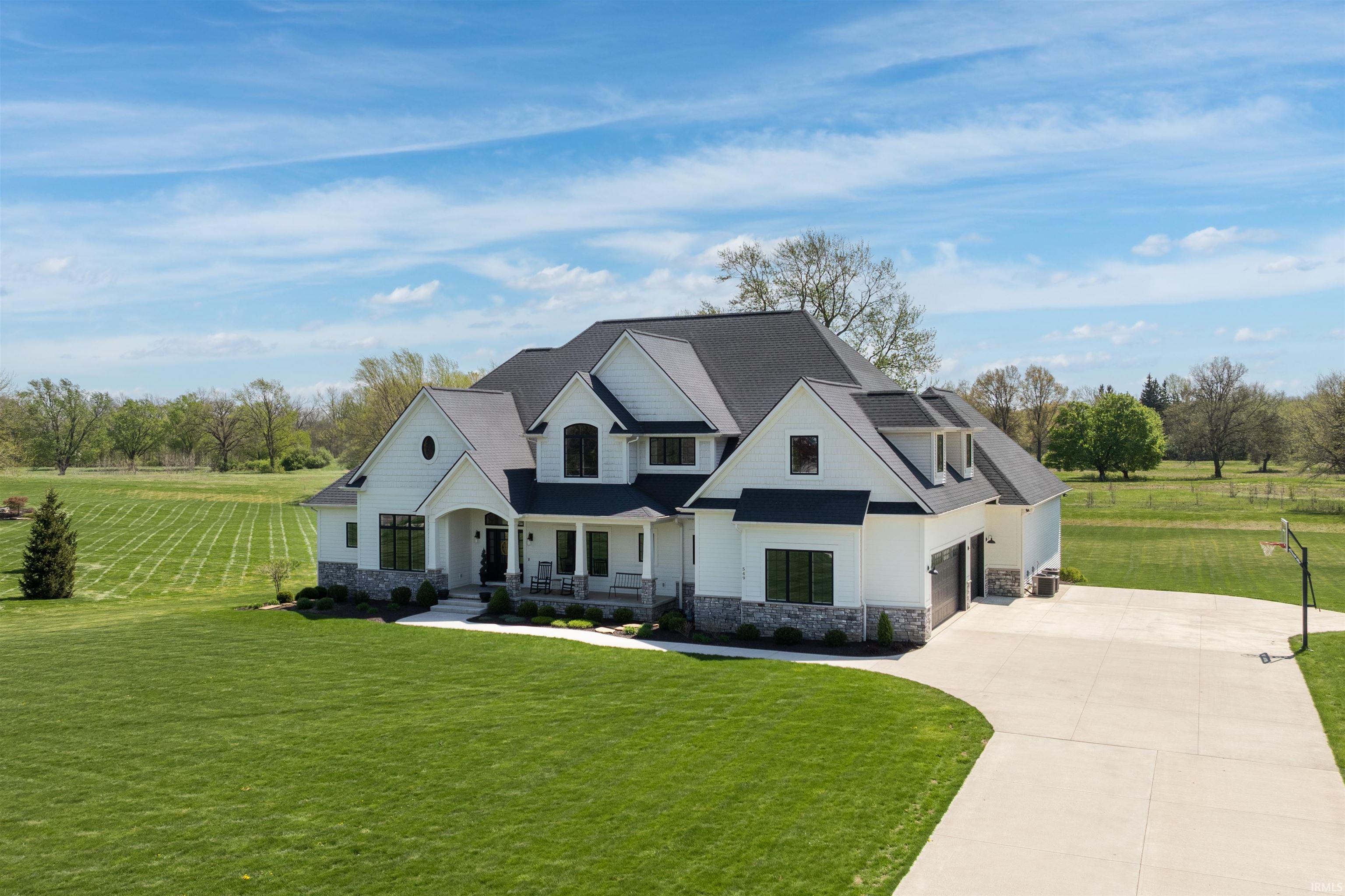 Expansive custom residence featuring white board-and-batten siding with stone accents, a multi-gabled dark shingle roof, and a three-car garage