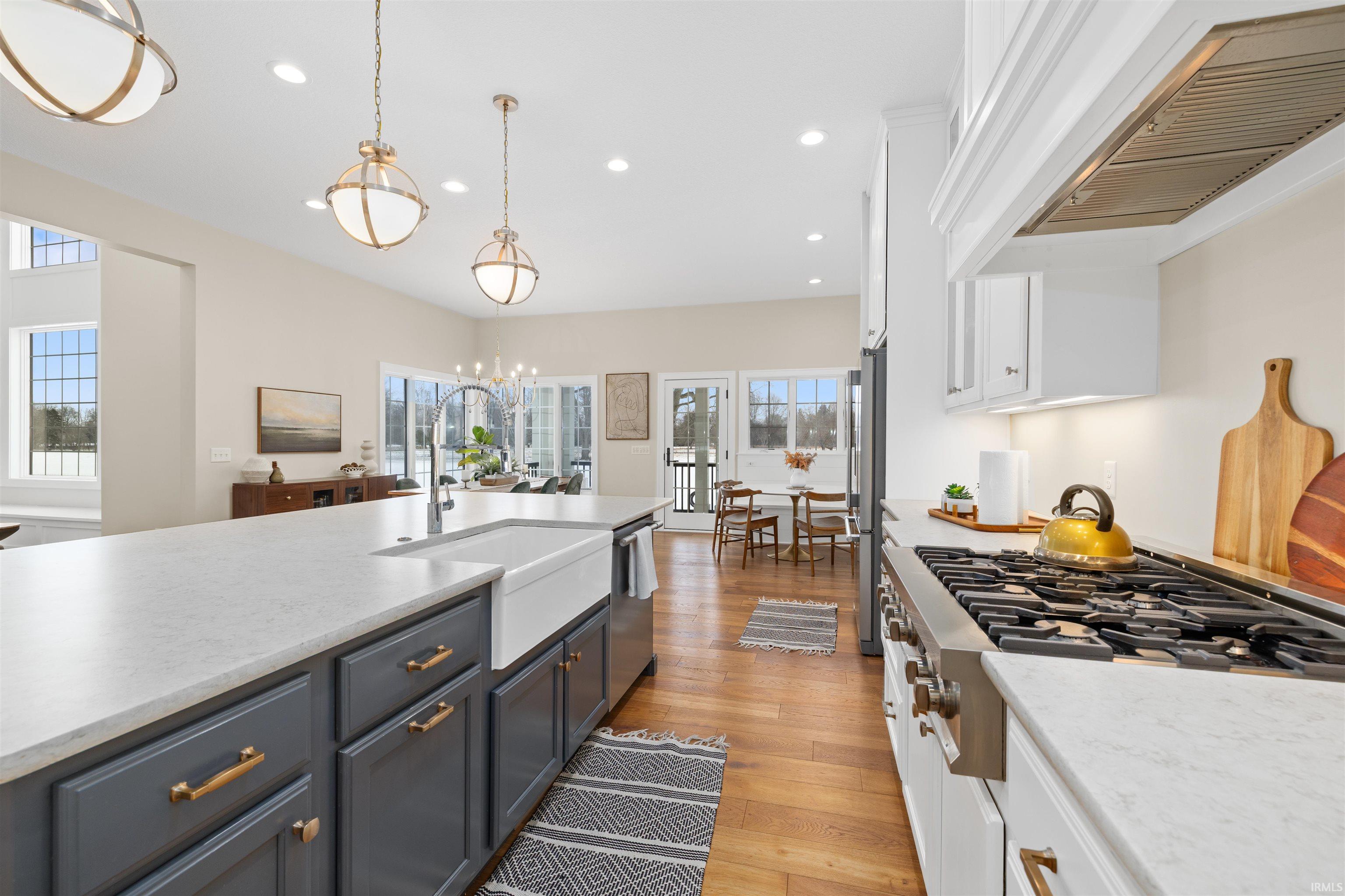 Kitchen with white cabinetry, stainless steel appliances, custom range hood, light stone countertops, and recessed lighting