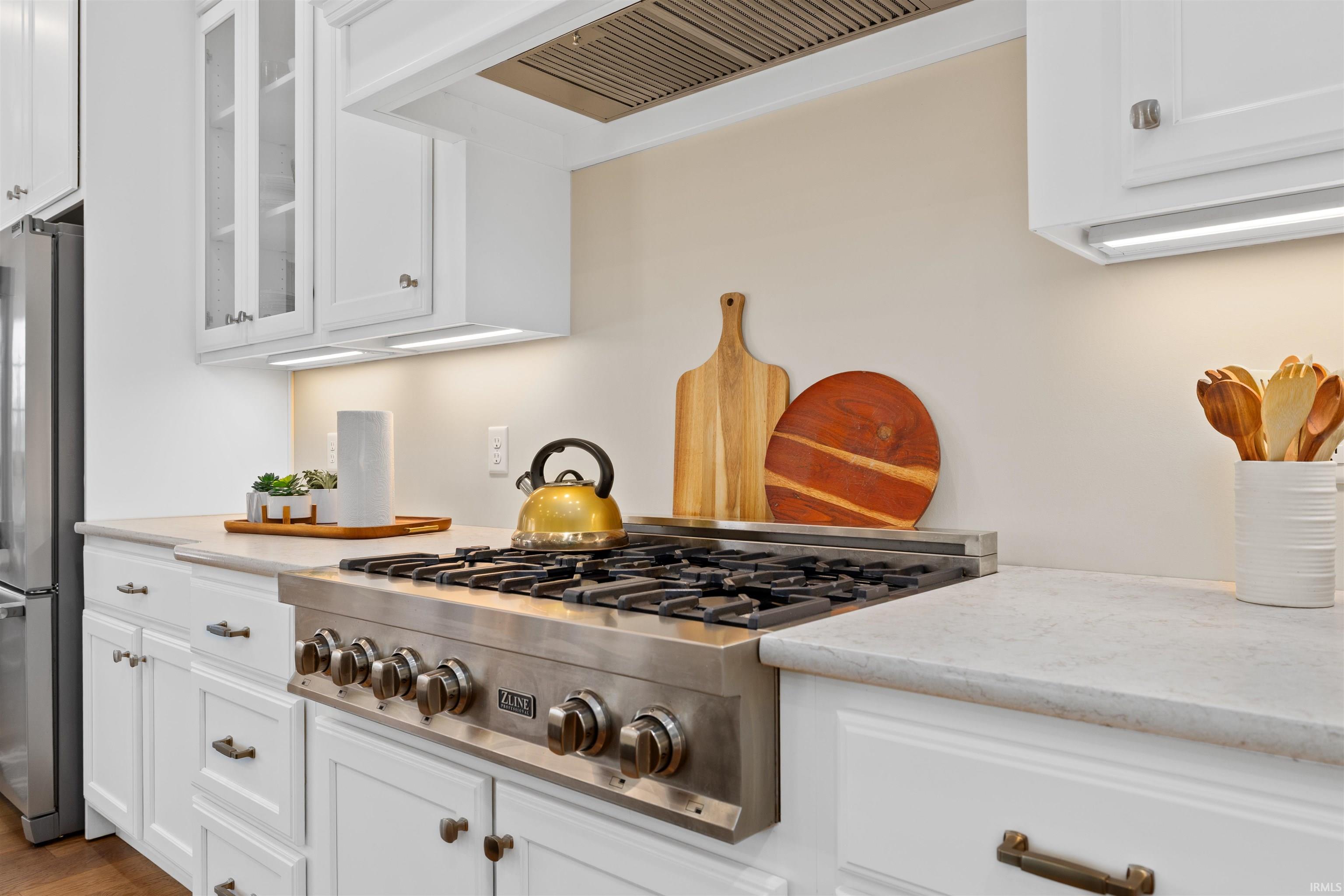 Kitchen featuring stainless steel appliances, white cabinetry, custom exhaust hood, and light stone counters