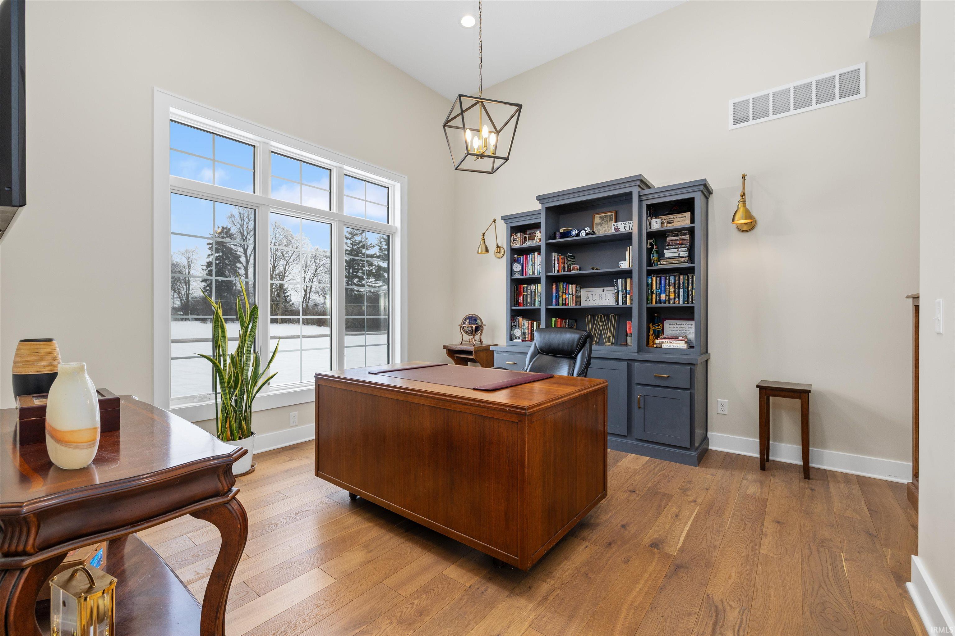 Office space with a towering ceiling, light wood-style floors, and a chandelier