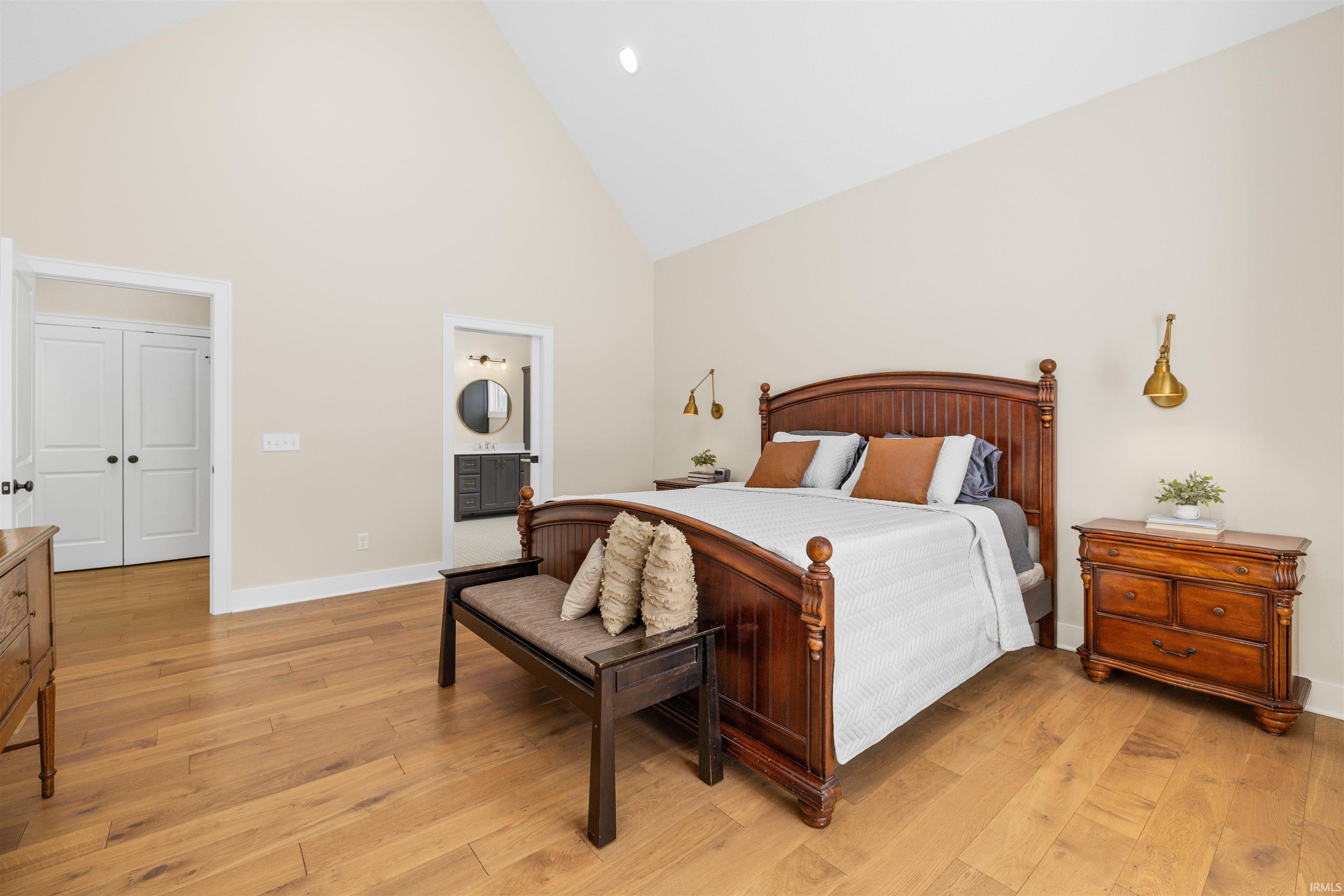 Bedroom with high vaulted ceiling, light wood-type flooring, and ensuite bath