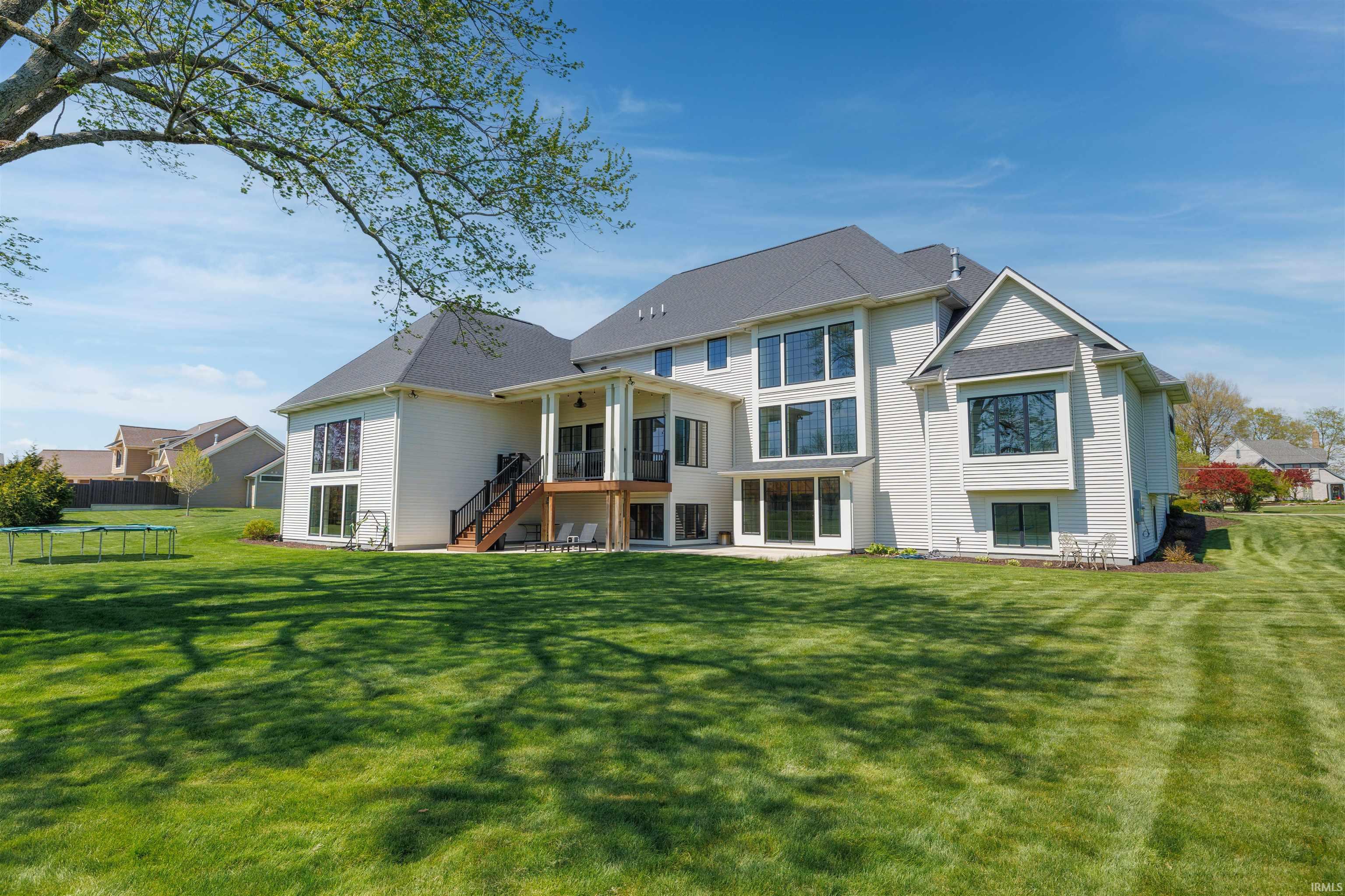 Expansive rear elevation featuring multiple large windows, a covered patio, an open-air deck with stairs, a walk-out lower level, and a large manicured lawn
