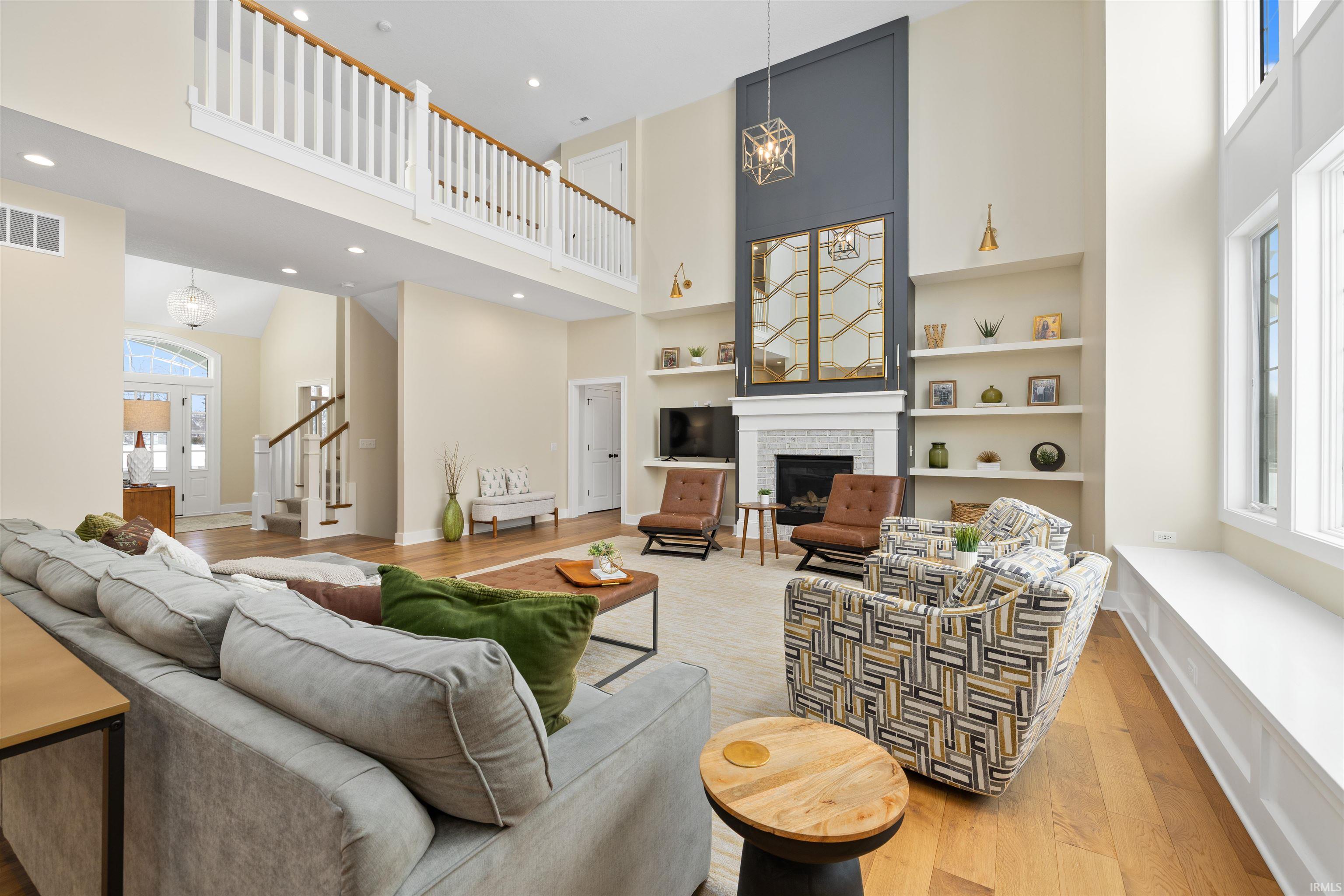 Living room with built in features, light wood-style floors, a fireplace, a towering ceiling, and a chandelier