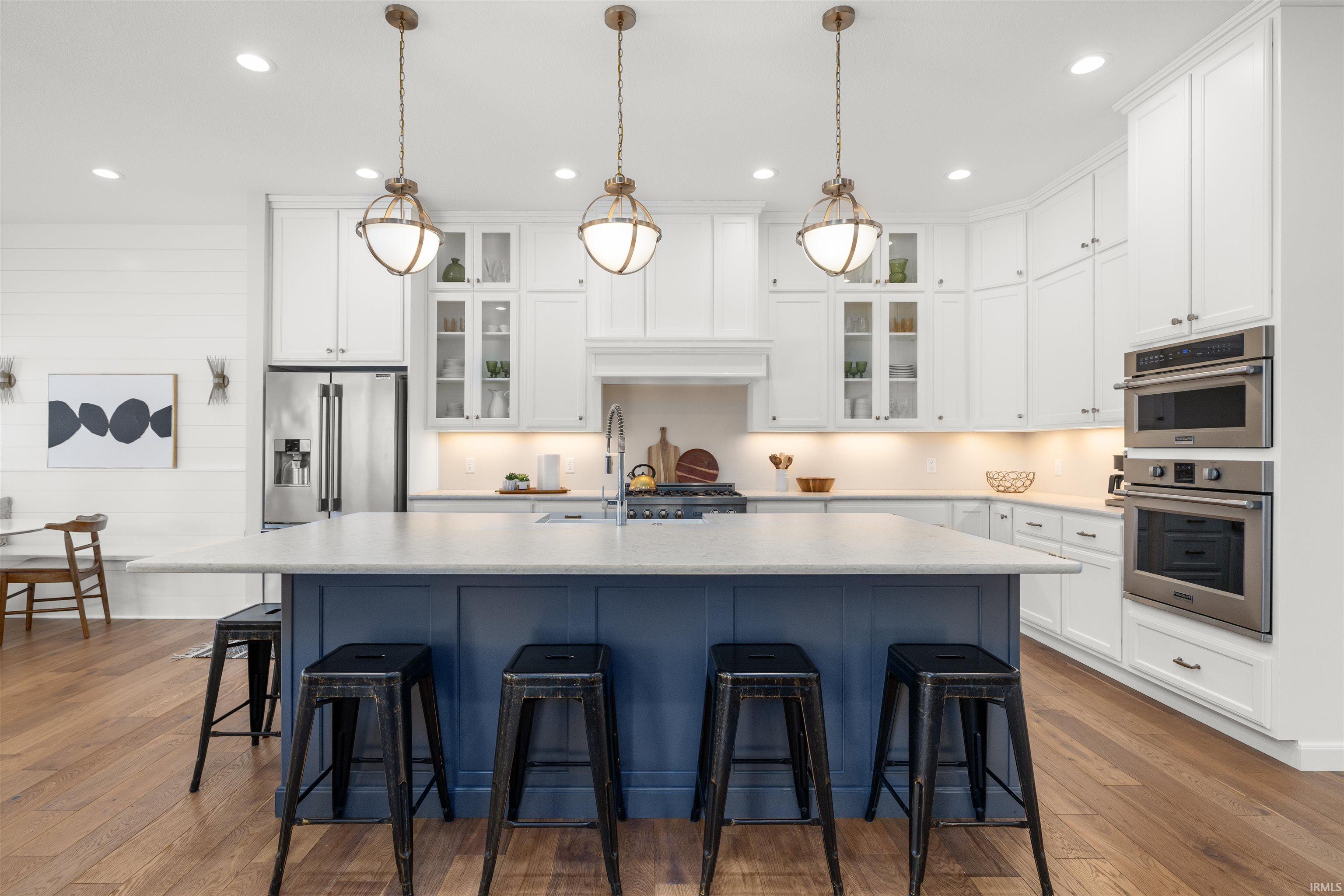 Kitchen with blue cabinetry, white cabinets, an island with sink, glass insert cabinets, and recessed lighting