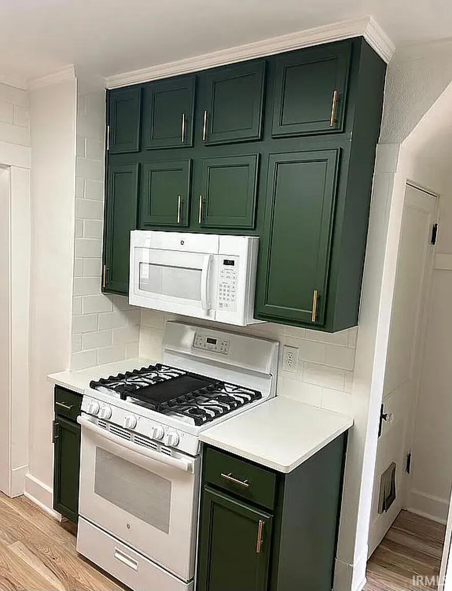Kitchen featuring green cabinets, white appliances, and tasteful backsplash
