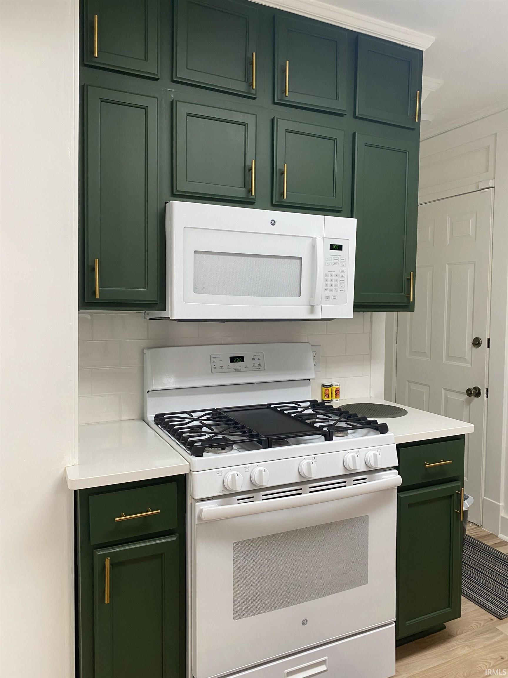 Kitchen featuring green cabinetry, white appliances, tasteful backsplash, light wood finished floors, and light stone countertops