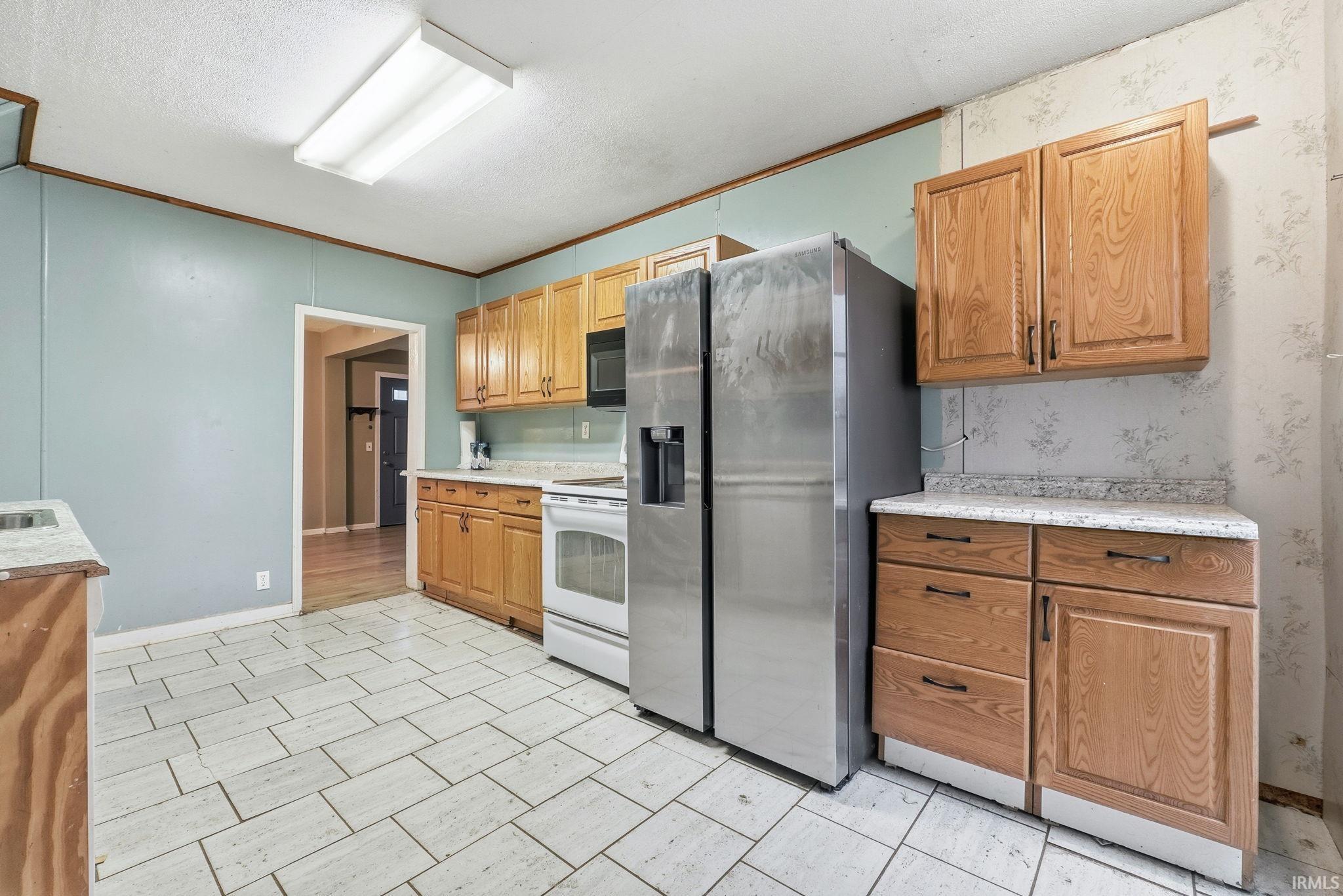 Kitchen with light countertops, stainless steel refrigerator with ice dispenser, crown molding, white range with electric stovetop, and brown cabinets