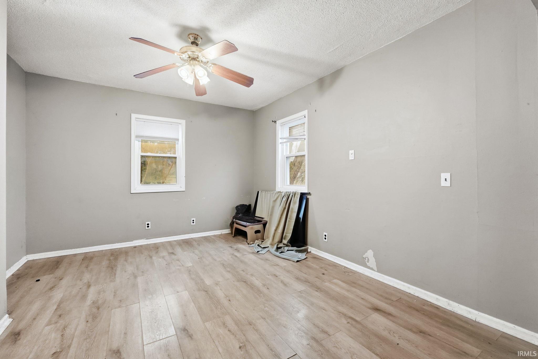 Empty room featuring light wood finished floors, a textured ceiling, and a ceiling fan